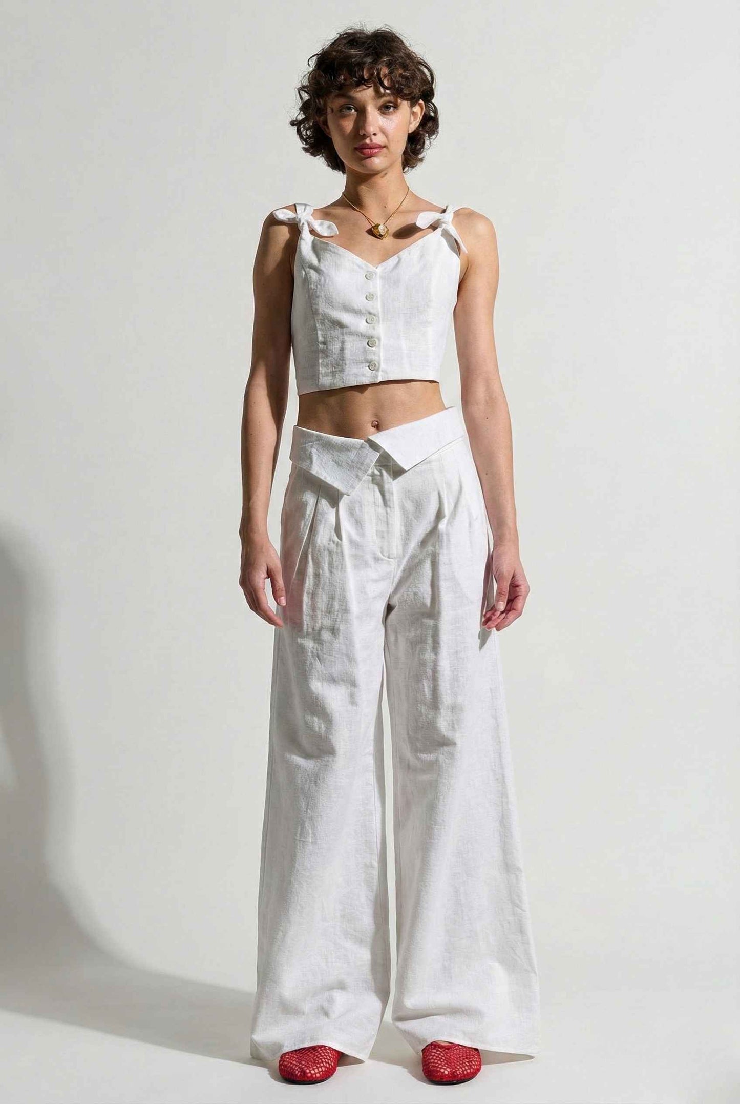 Woman wearing a Aria Top White Linen Blend Button Front Tie Crop Top and wide-leg pants against a plain background