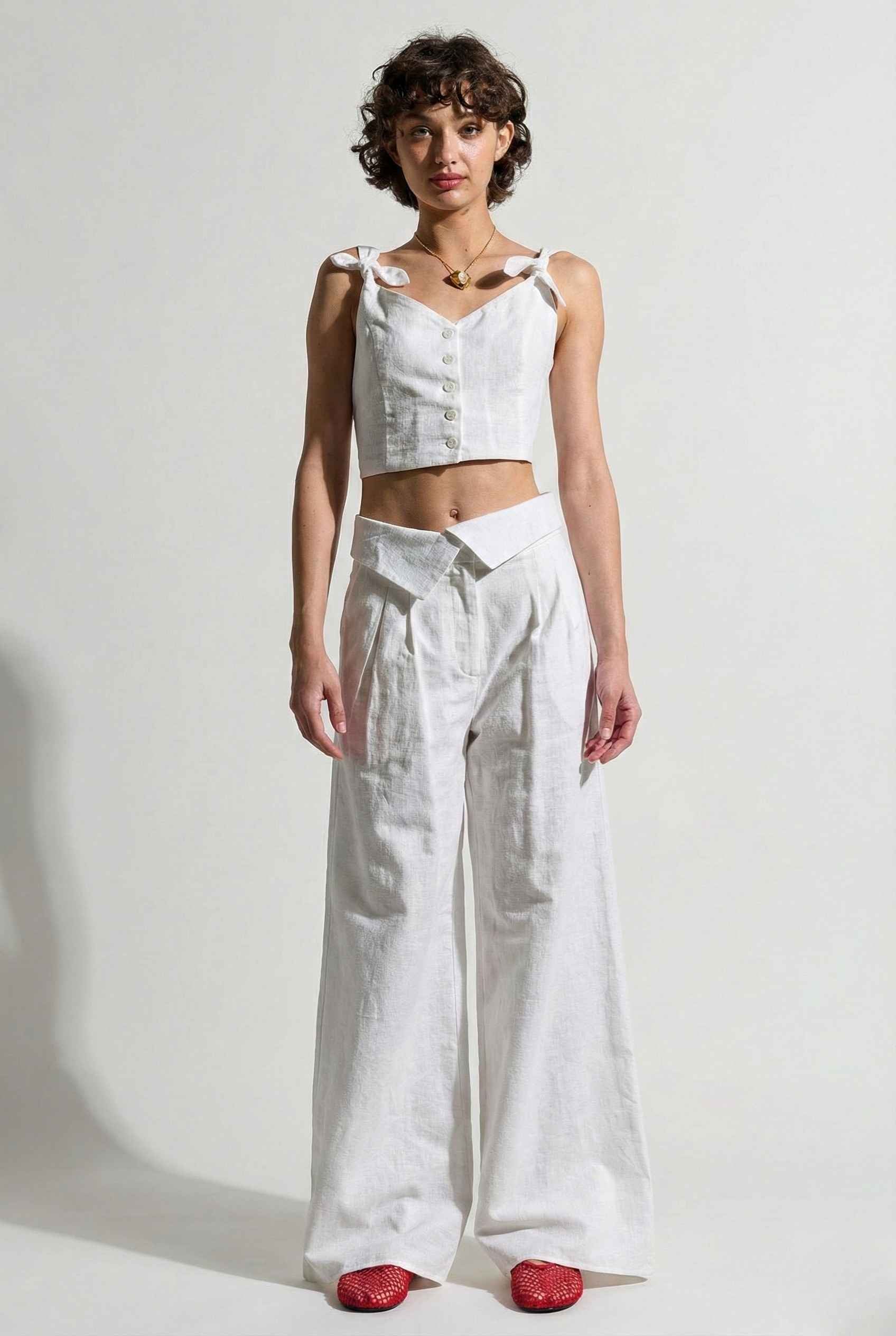 Woman wearing a Aria Top White Linen Blend Button Front Tie Crop Top and wide-leg pants against a plain background
