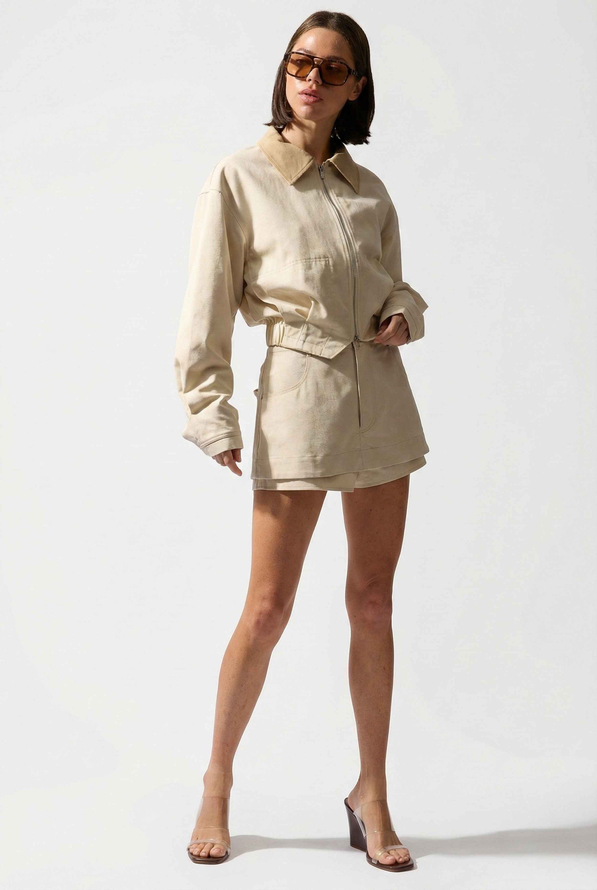 Model wearing Arlo Jacket | Beige Lyocell-Blend Jacket with Contrast Collar with striped shirt and shorts and wedge heels