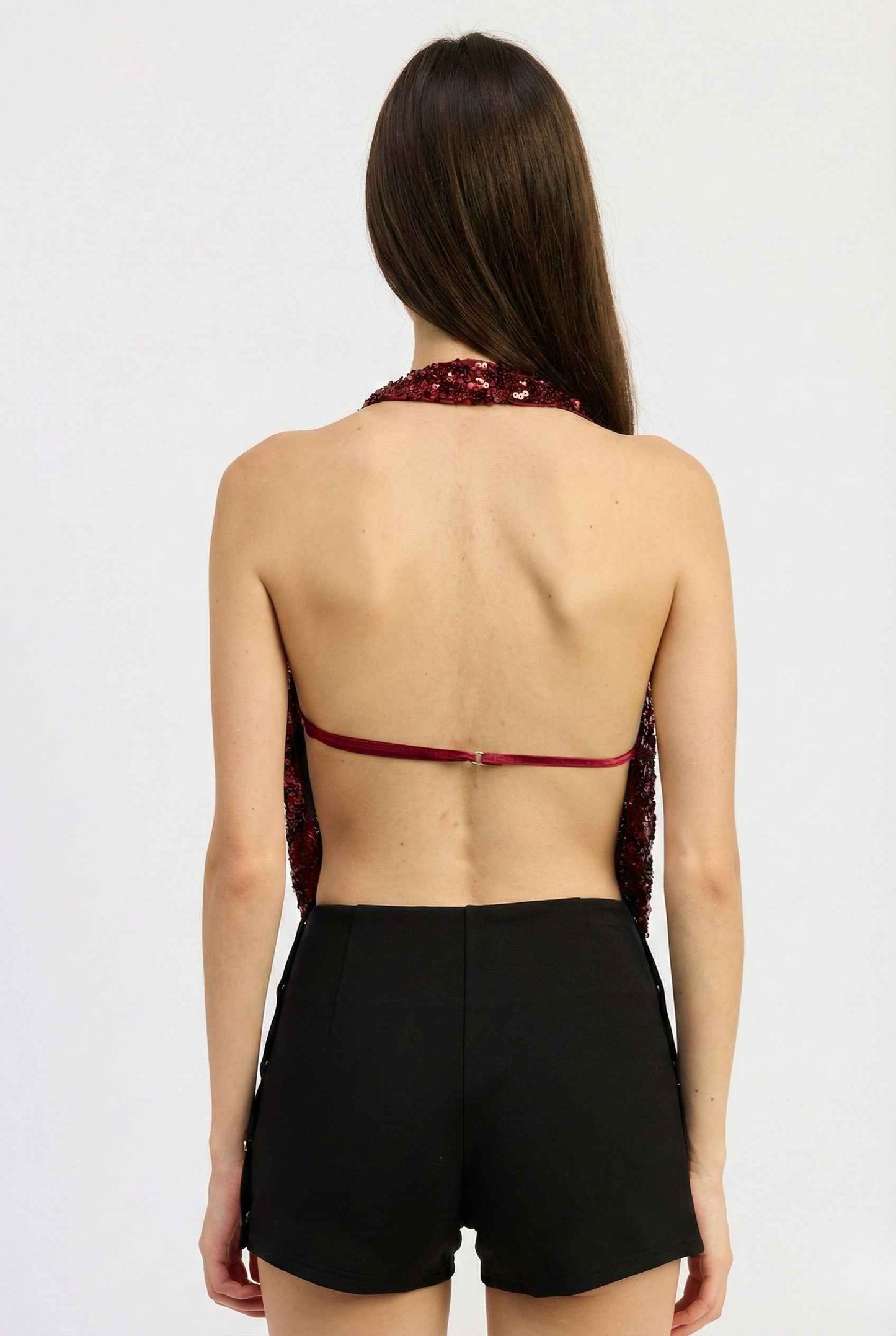 Woman wearing a Astra Top Cherry Sequin Draped Halter Neck with lace details and black shorts on a white background