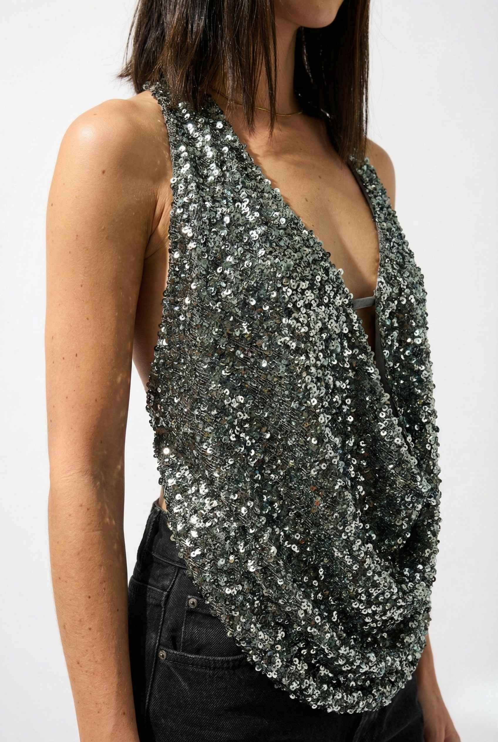 Woman wearing a Astra Top Silver Sequin Draped Halter Neck against a white background