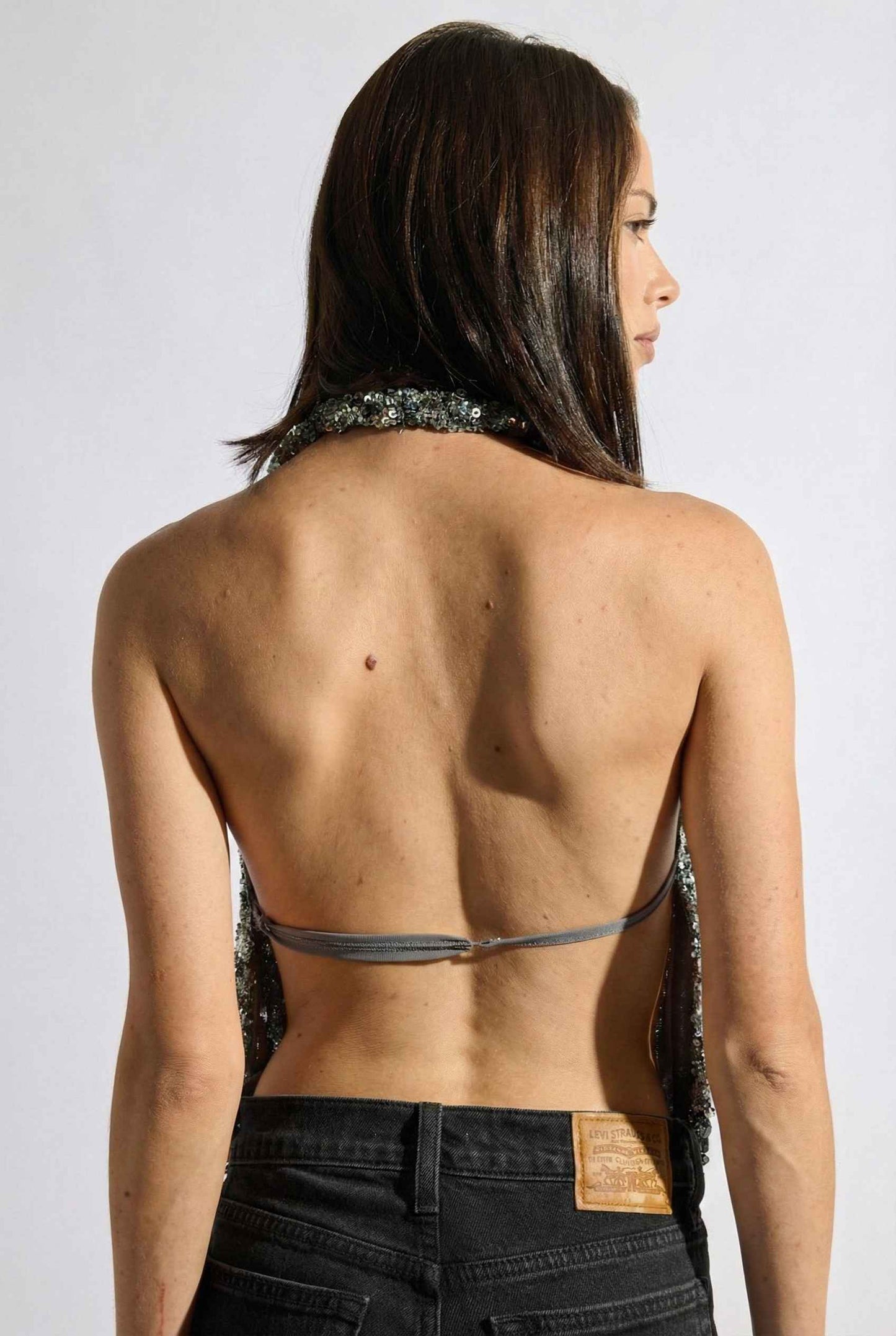 Woman wearing a Astra Top Silver Sequin Draped Halter Neck with a plain background