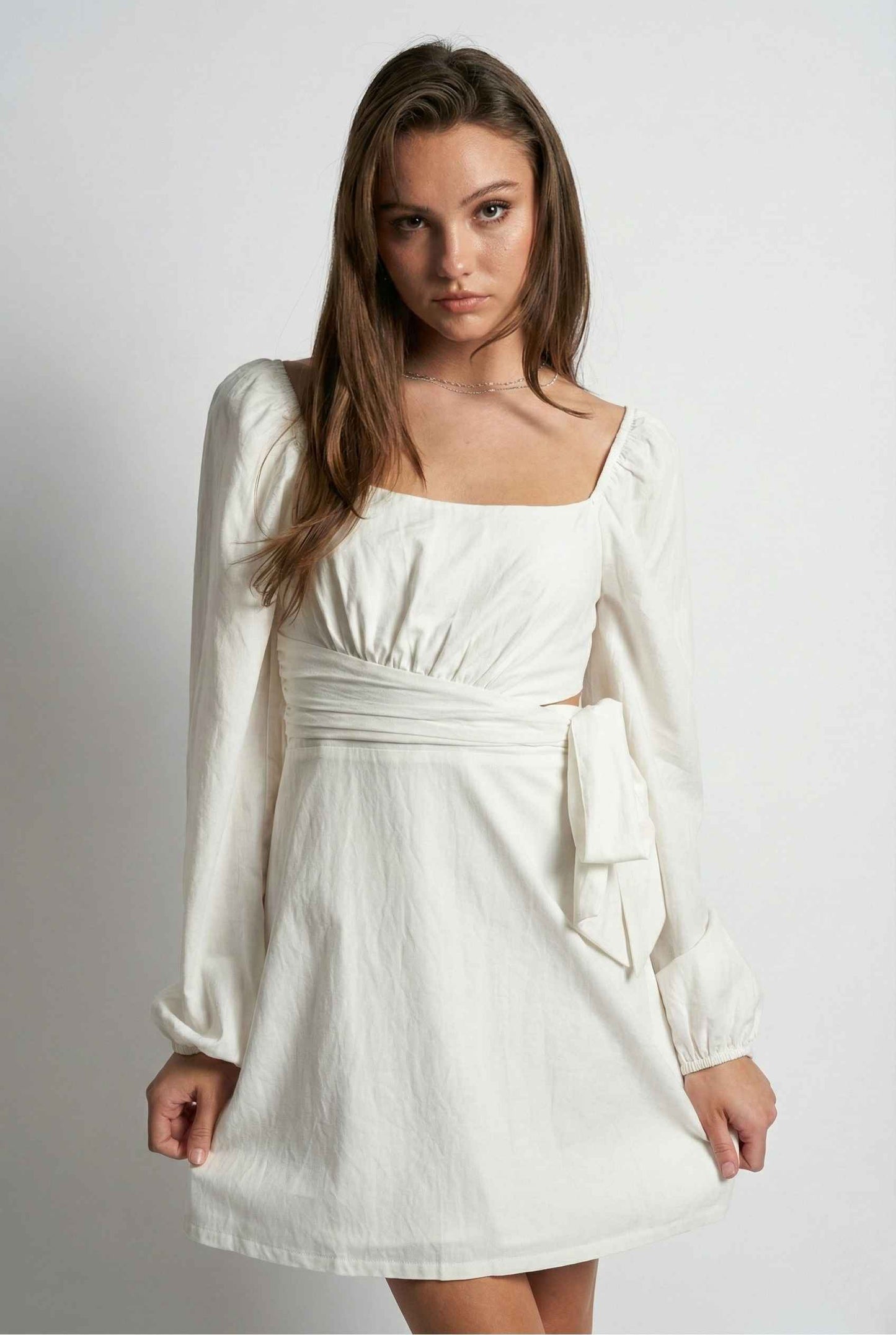 Woman wearing a Aurelia Mini White Long Sleeve Cutout Dress with long sleeves against a plain background