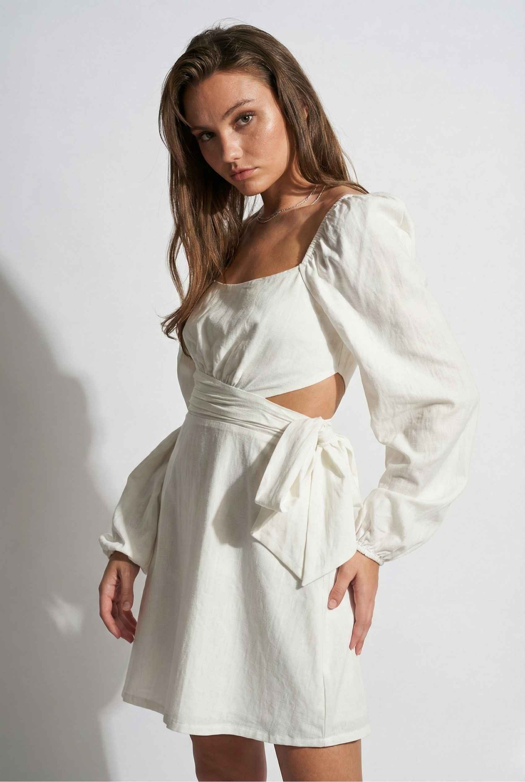Woman wearing a Aurelia Mini White Long Sleeve Cutout Dress with cut-out design against a plain background