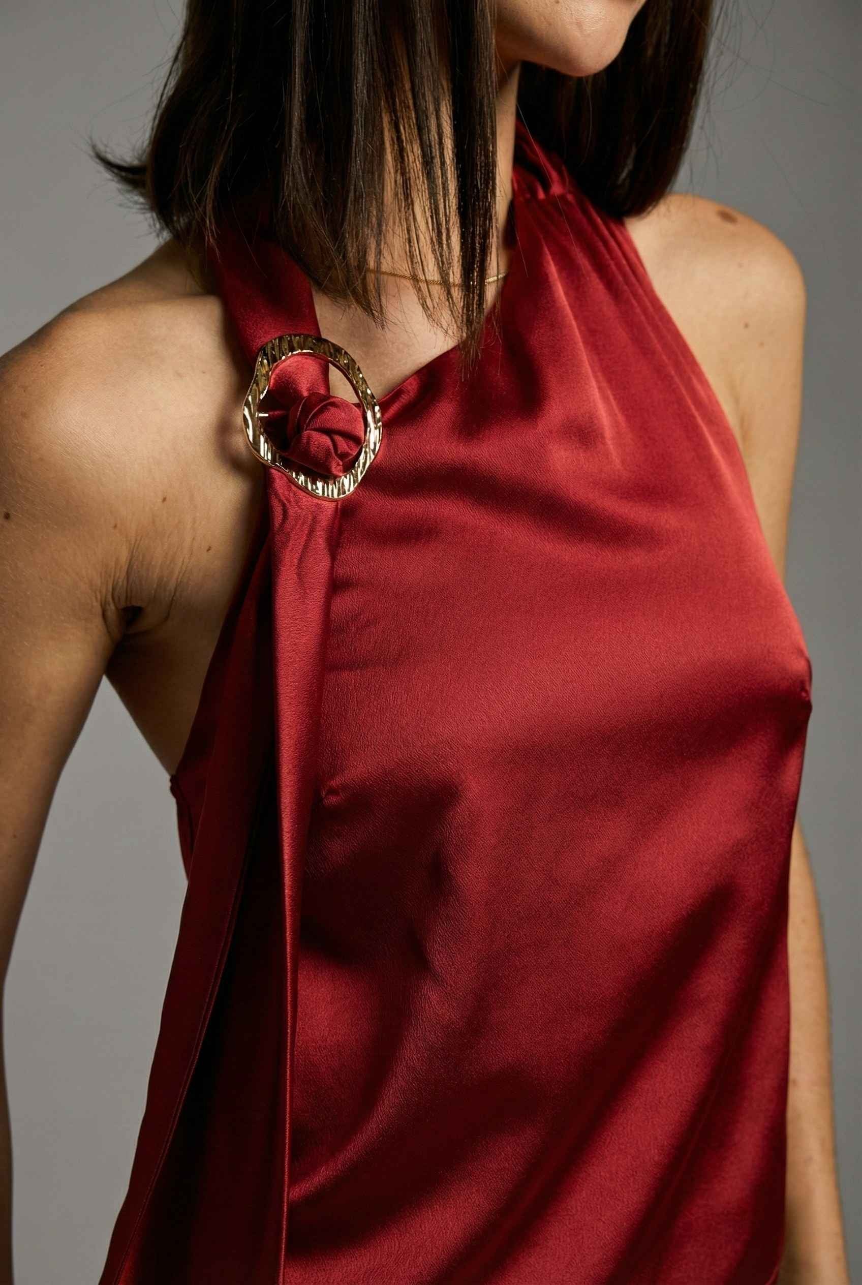 Aurelia Top Burgundy Satin One-Shoulder Scarf Blouse with a gold ring detail on a gray background