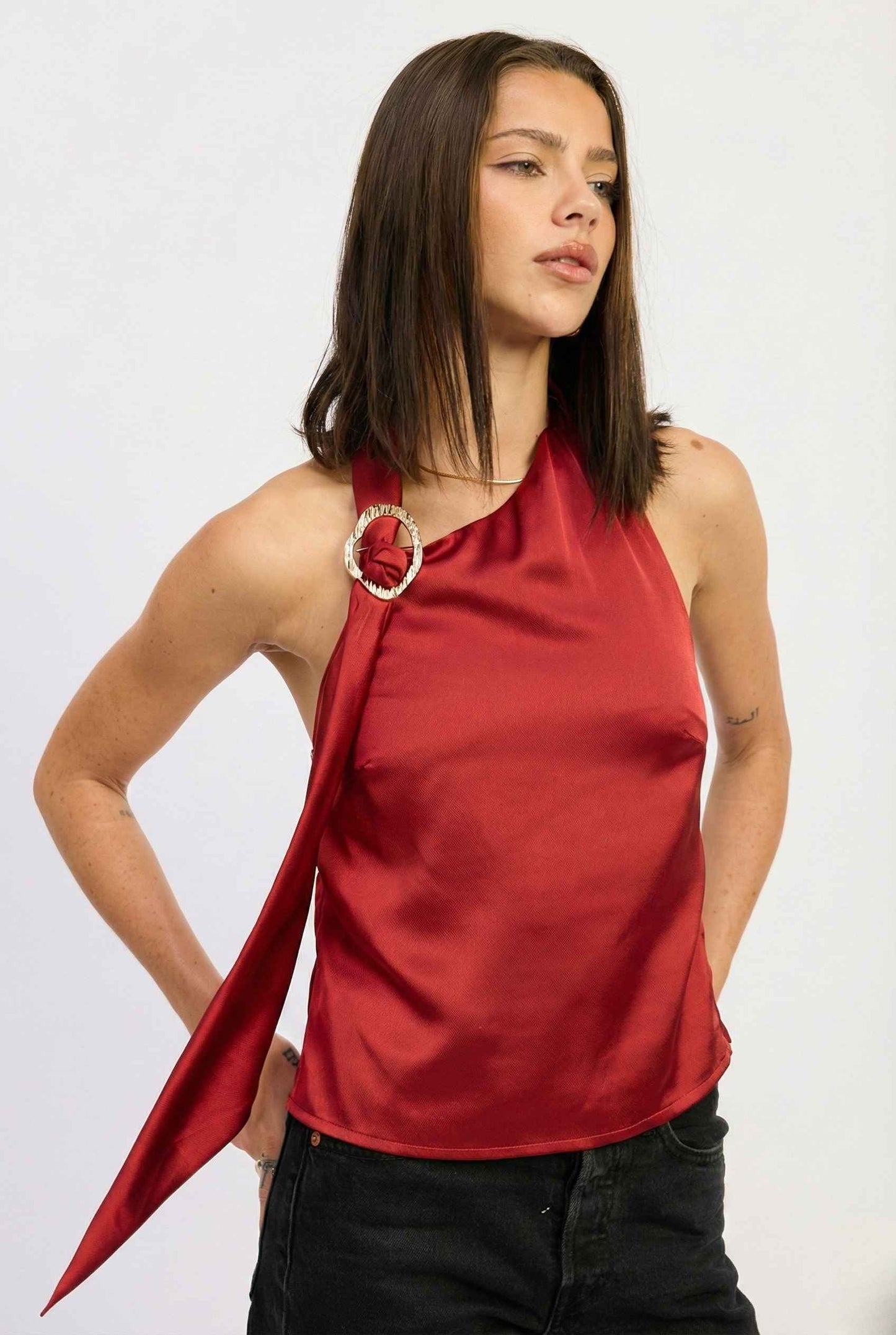 Woman wearing a Aurelia Top Burgundy Satin One-Shoulder Scarf Blouse with a gold ring detail on a white background
