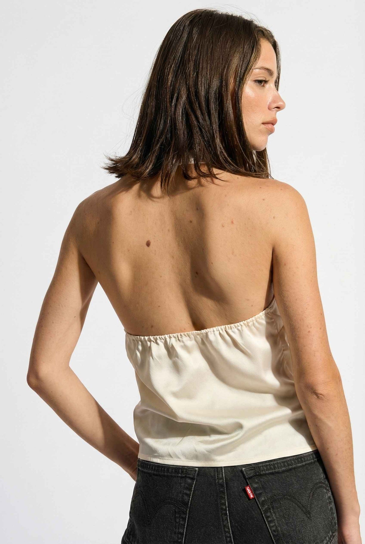 Woman wearing a Aurelia Top Ivory Satin One-Shoulder Scarf Blouse and black pants on a white background