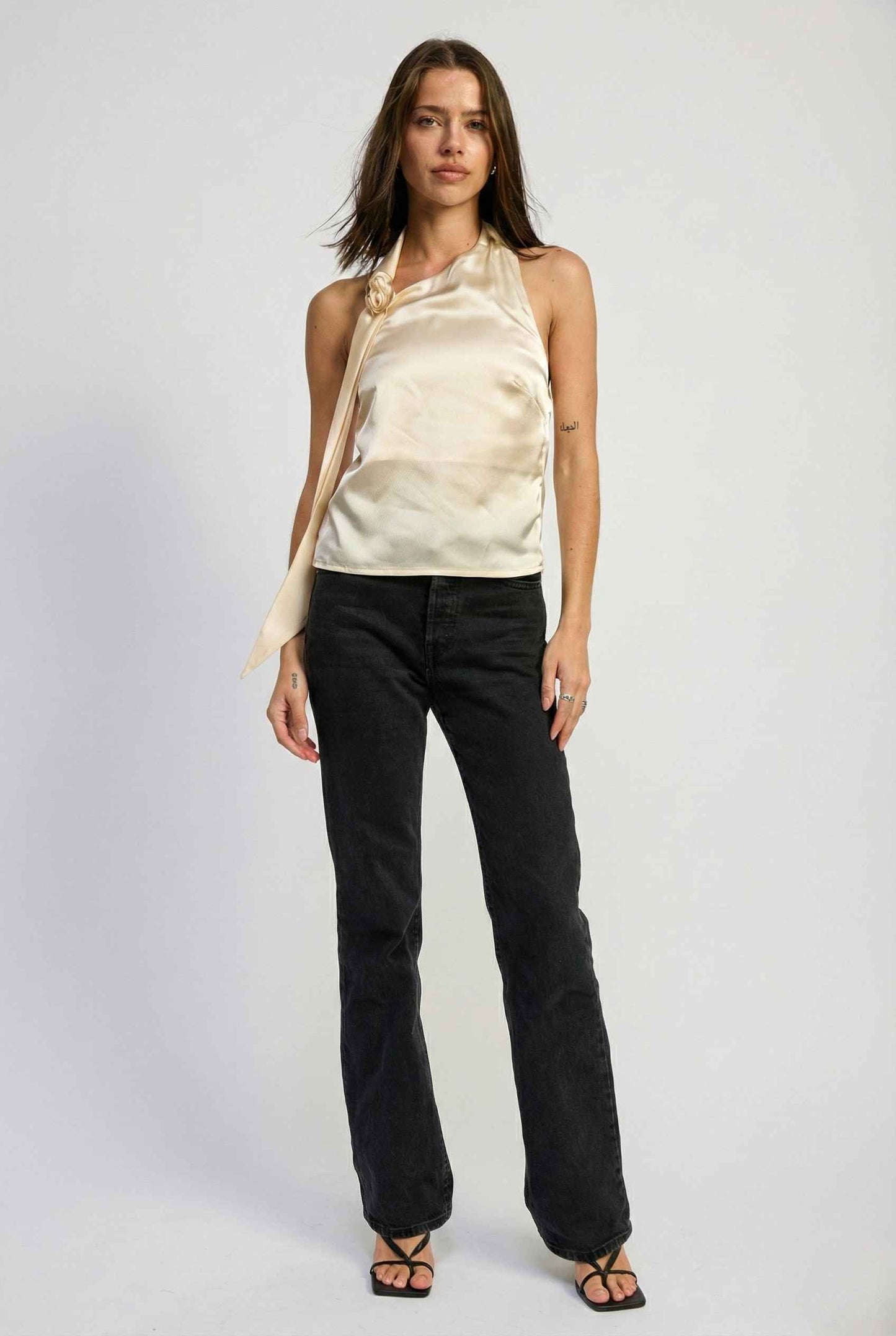 Woman wearing a Aurelia Top Ivory Satin One-Shoulder Scarf Blouse and black pants on a white background