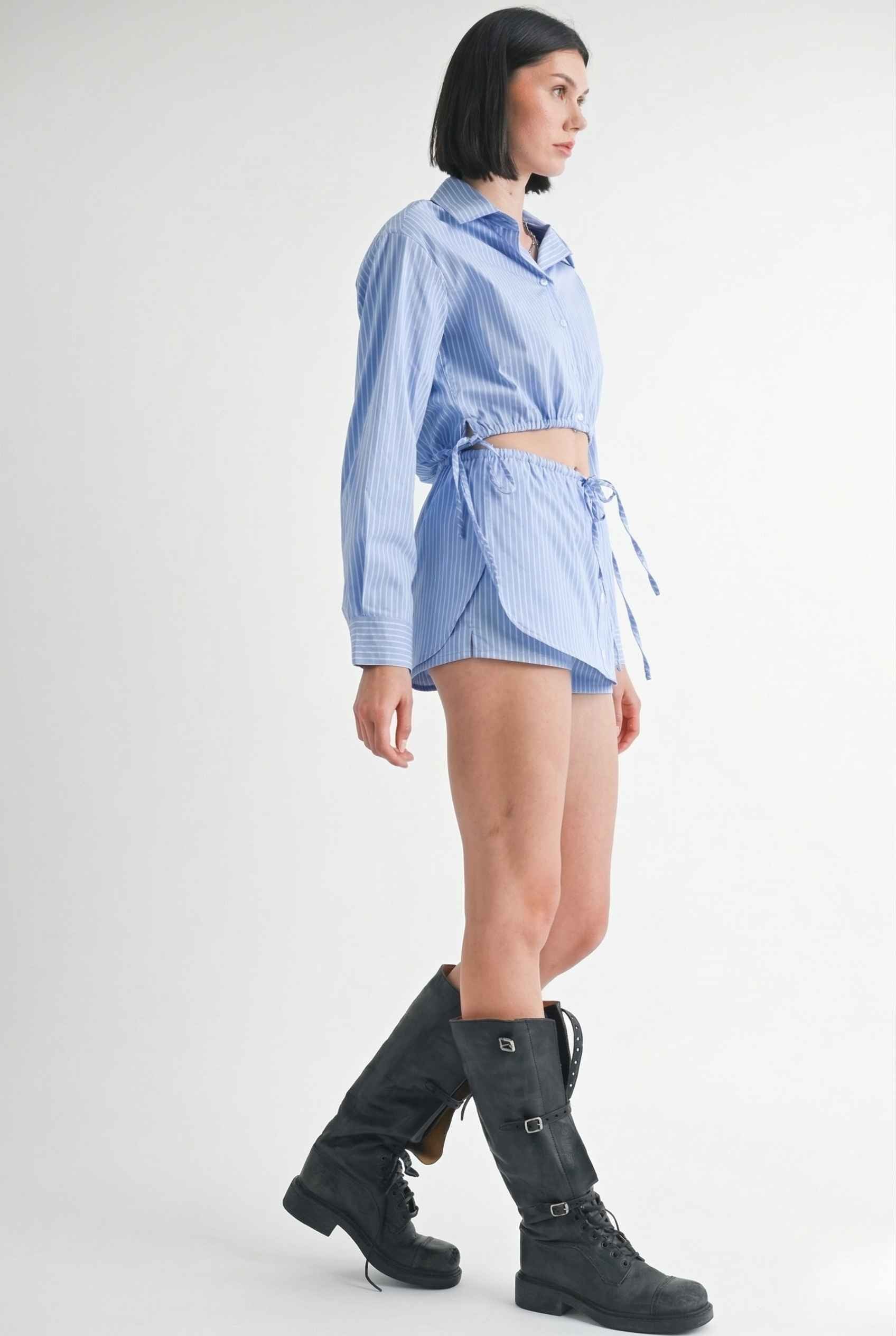 Woman wearing a Blair Skort Blue Striped Poplin Mini Skort with Shirttail Hem with black boots on a plain background