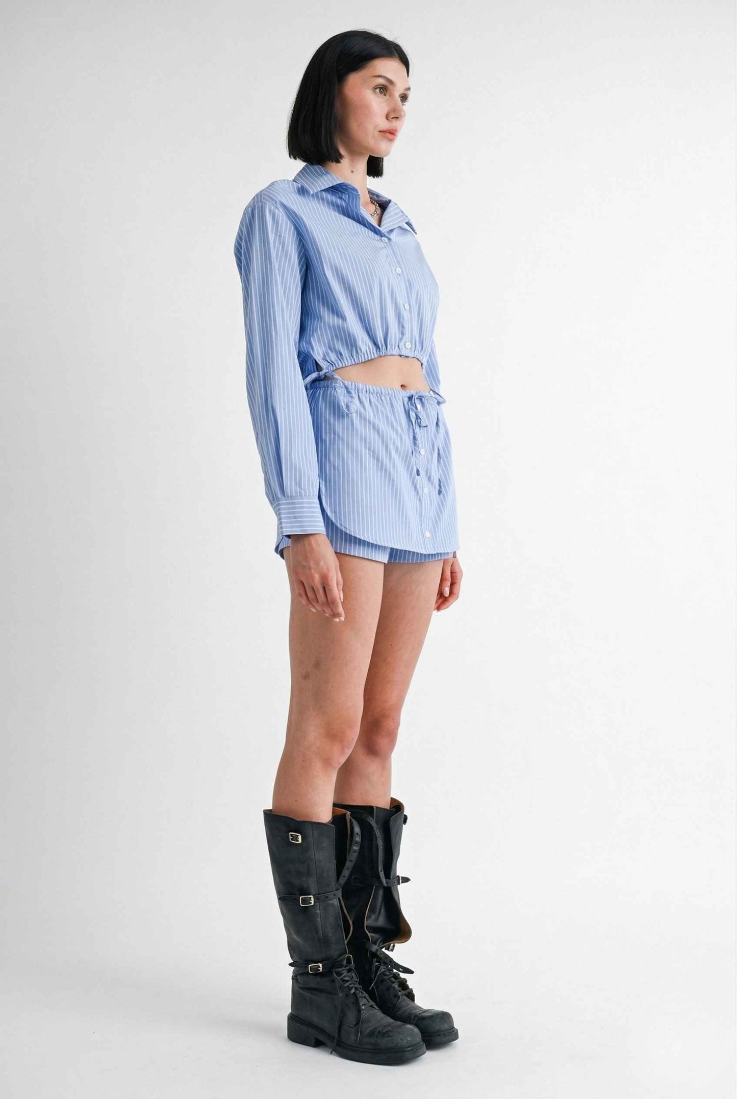 Woman wearing a Blair Skort Blue Striped Poplin Mini Skort with Shirttail Hem with black boots on a plain background