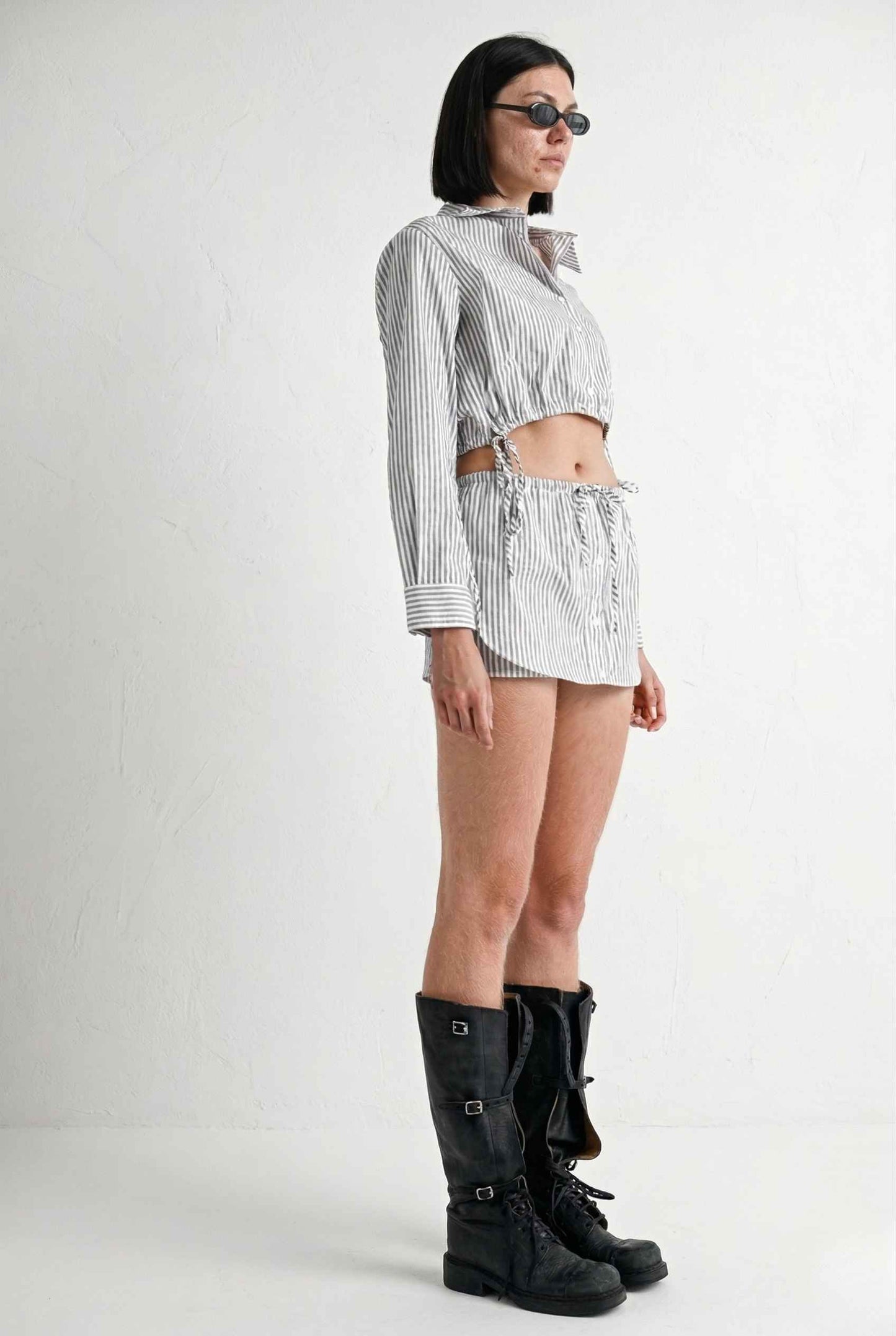 Woman wearing a striped shirt, Blair Skort White Striped Poplin Mini Skort with Shirttail Hem, and black boots on a white background