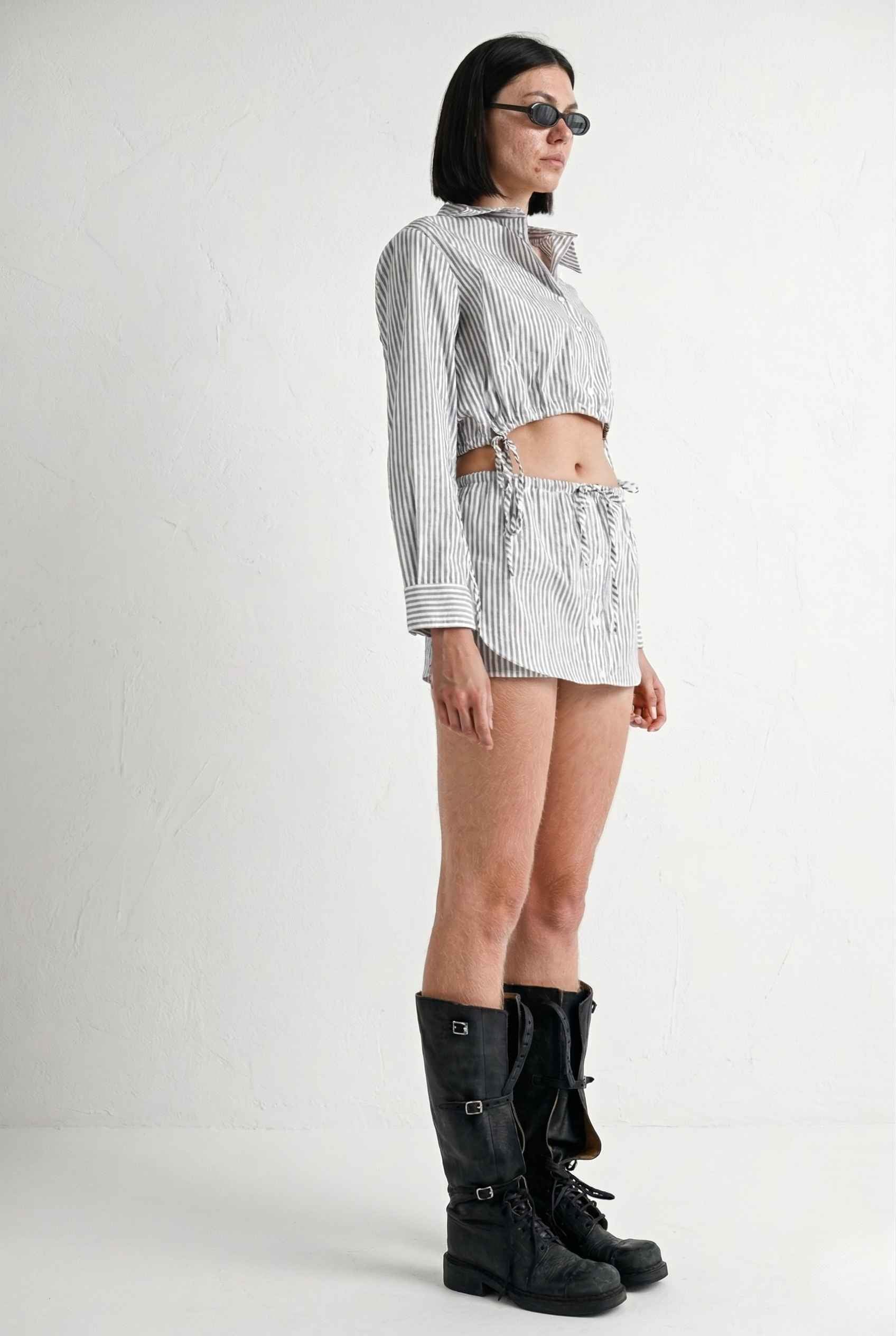 Woman wearing a striped shirt, Blair Skort White Striped Poplin Mini Skort with Shirttail Hem, and black boots on a white background