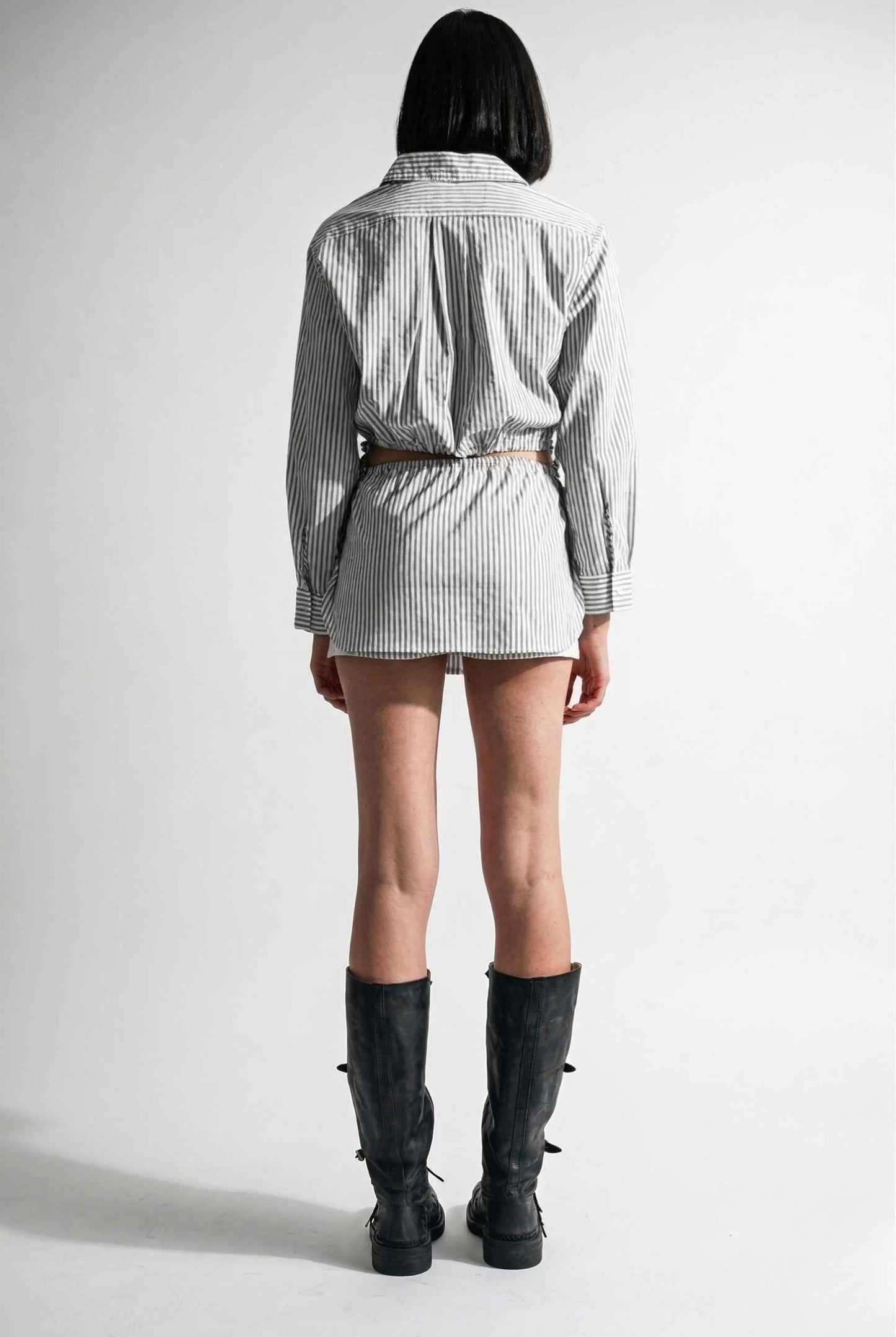 Woman wearing a checkered shirt, Blair Skort White Striped Poplin Mini Skort with Shirttail Hem, and black boots on a white background