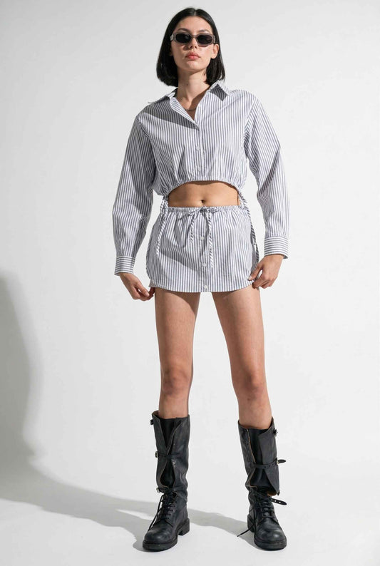 Woman wearing a black and white striped shirt and Blair Skort White Striped Poplin Mini Skort with Shirttail Hem with black boots on a white background