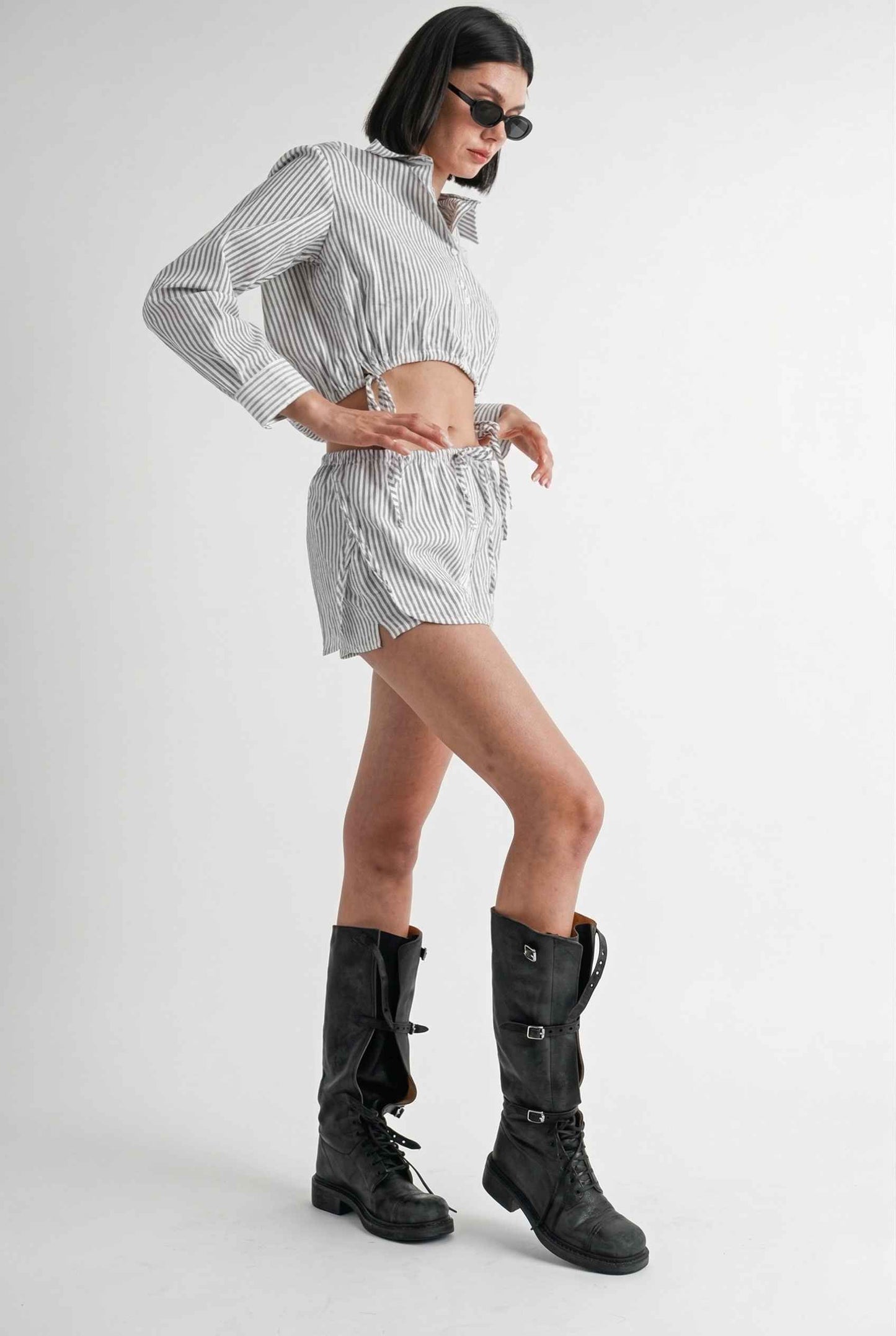 Woman wearing a Blair Skort White Striped Poplin Mini Skort with Shirttail Hem with high boots on a white background