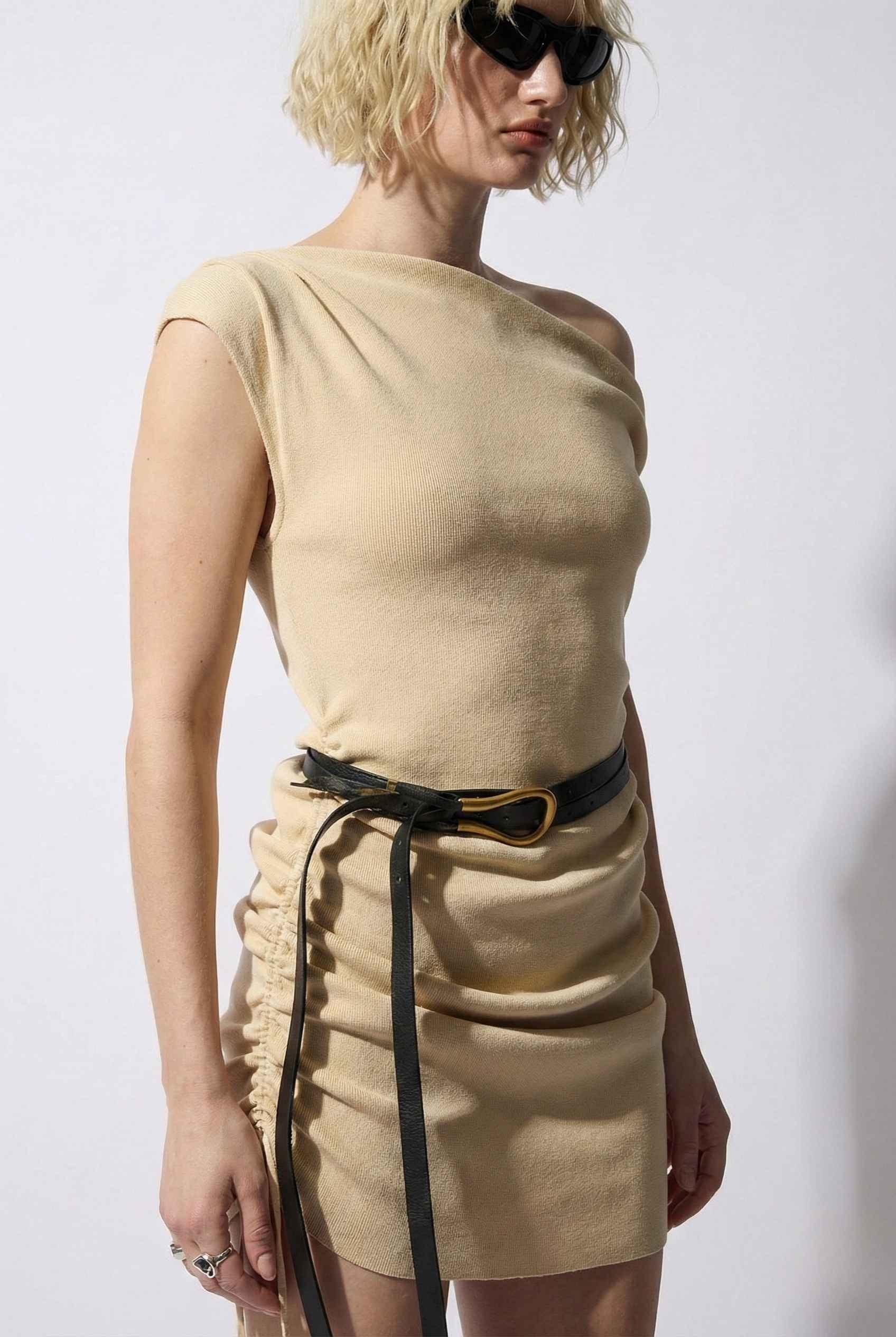 Woman wearing a Blaire Mini Cream Off-Shoulder Ruched Dress with a black belt against a white background