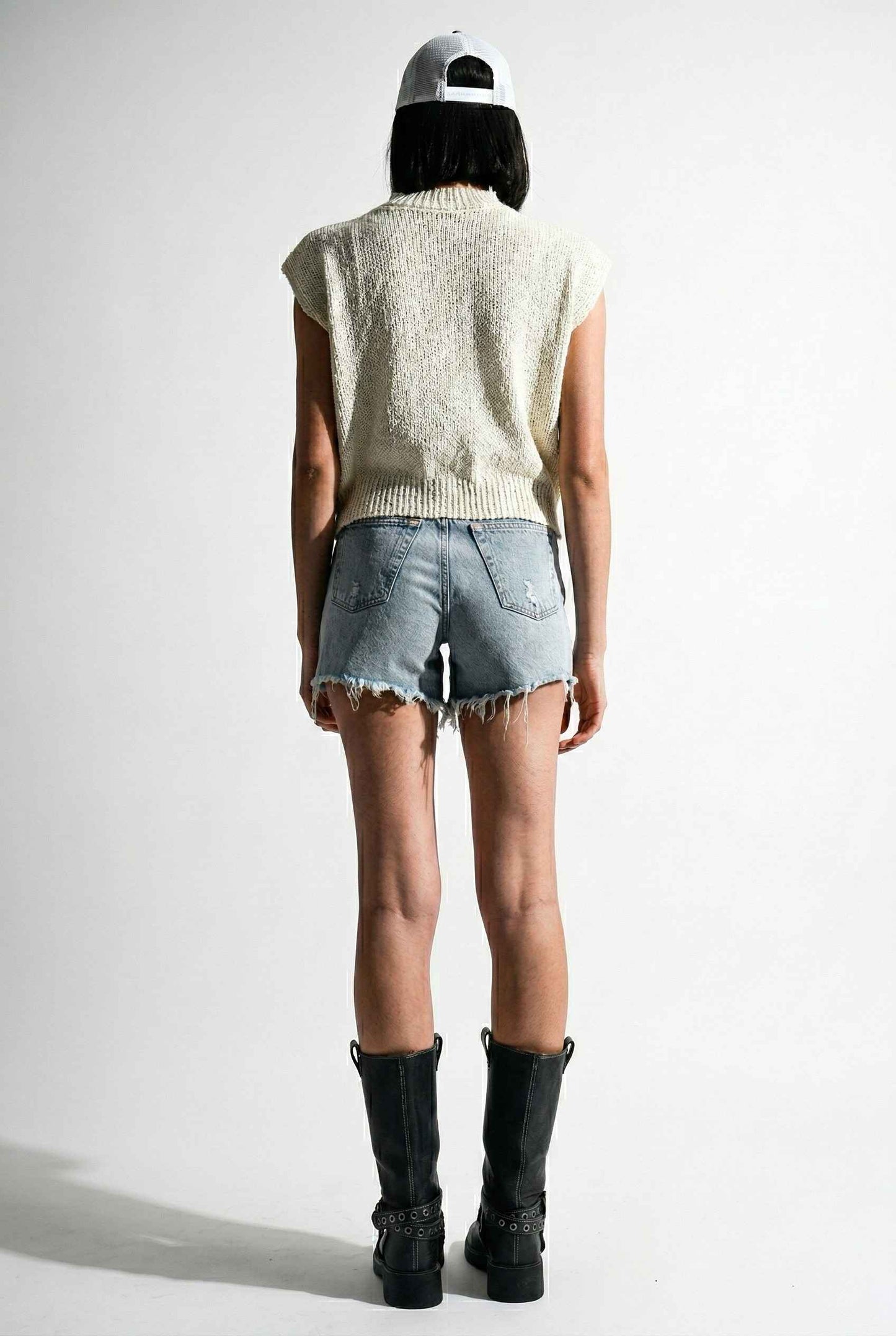 Model wearing Blaire Top in Off White Textured Knit Sleeveless Muscle Tee with denim shorts and tall boots on a plain background