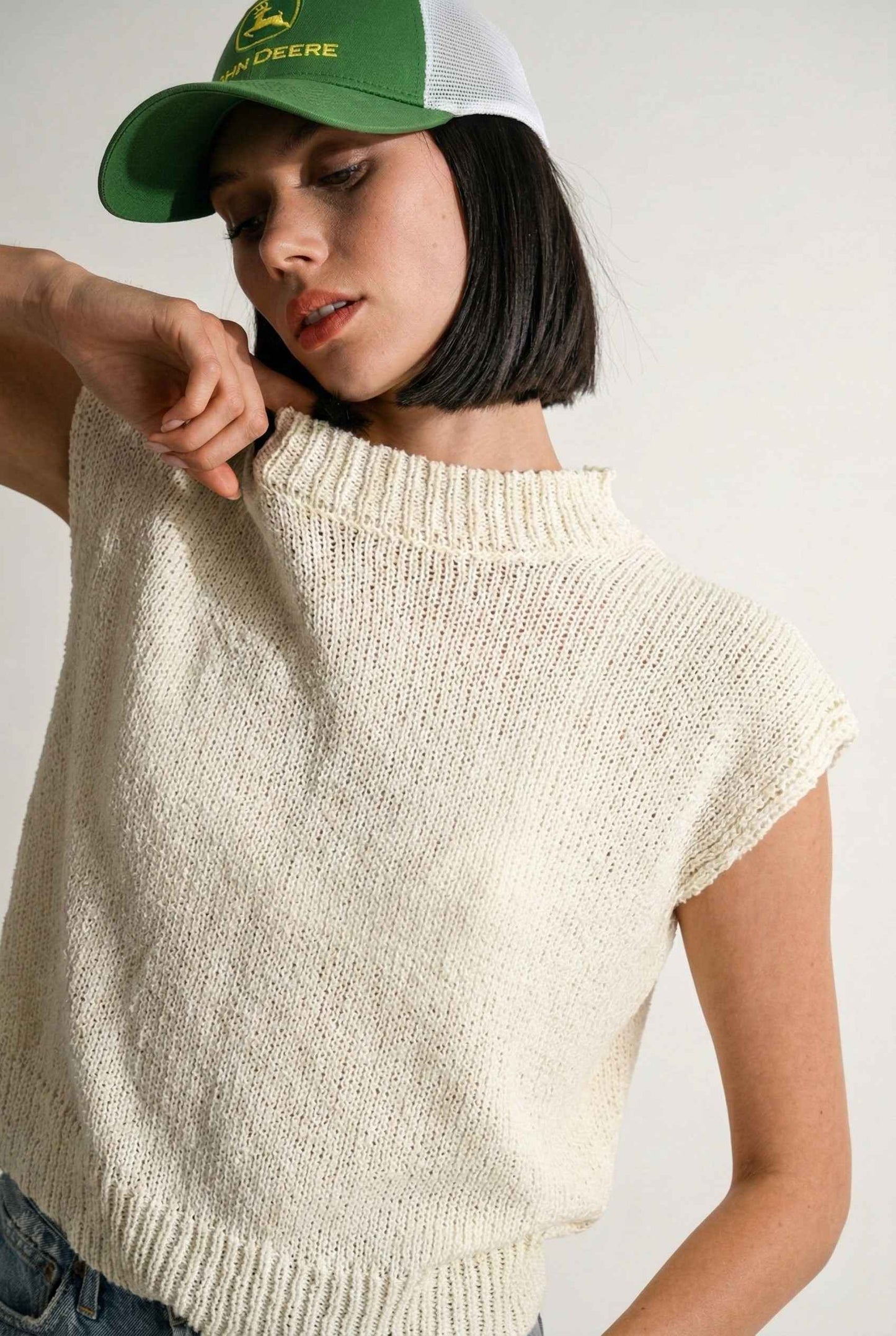 Model wearing Blaire Top in Off White Textured Knit Sleeveless Muscle Tee  and a ball cap on a plain background
