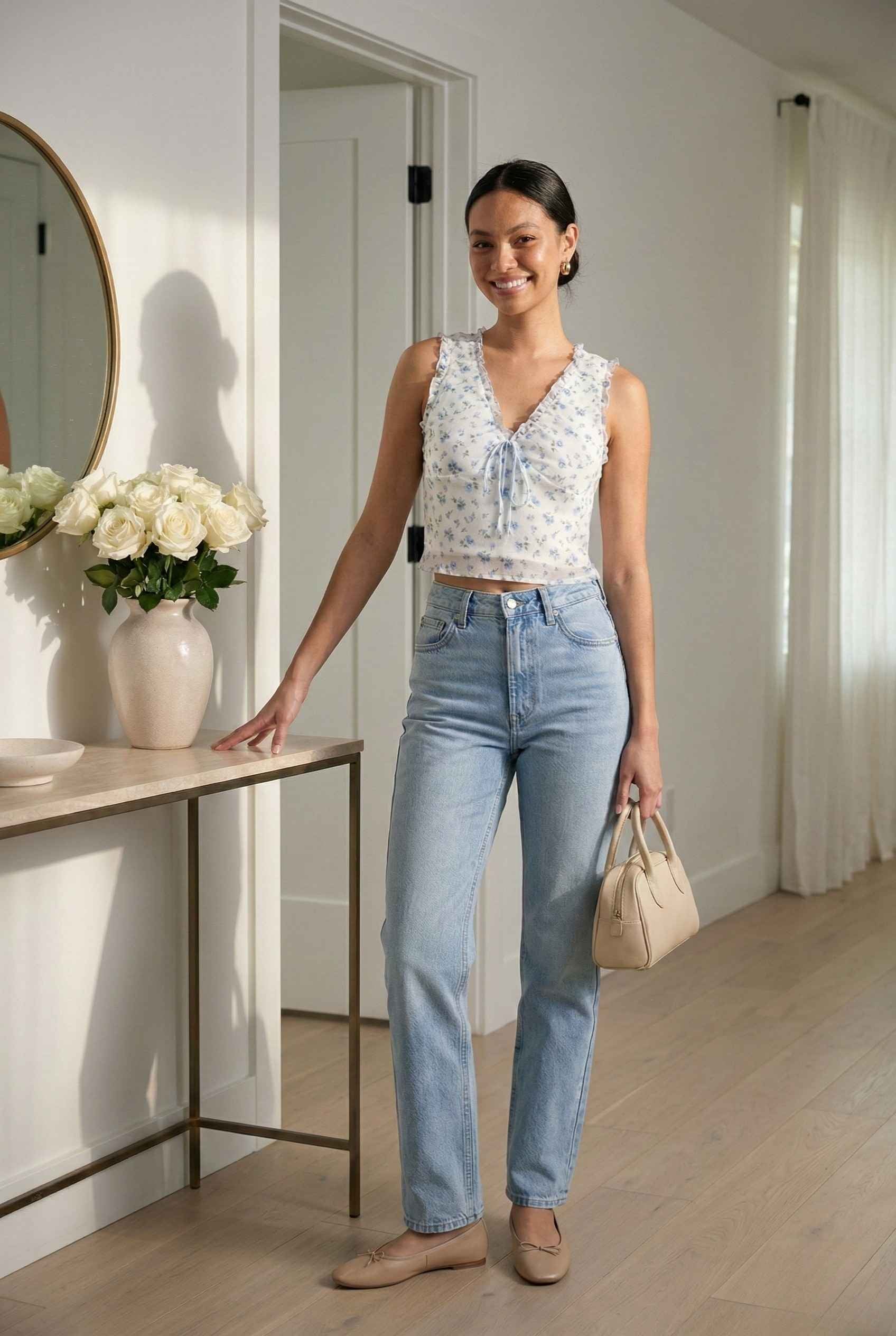 Woman in a Callie Top White & Light Blue Floral Ruffle Tie-Front Cami and blue jeans standing in a room with a table and flowers.