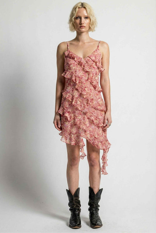 Woman wearing a Camille Mini Pink Asymmetrical Ruffle Floral Dress with black boots on a white background