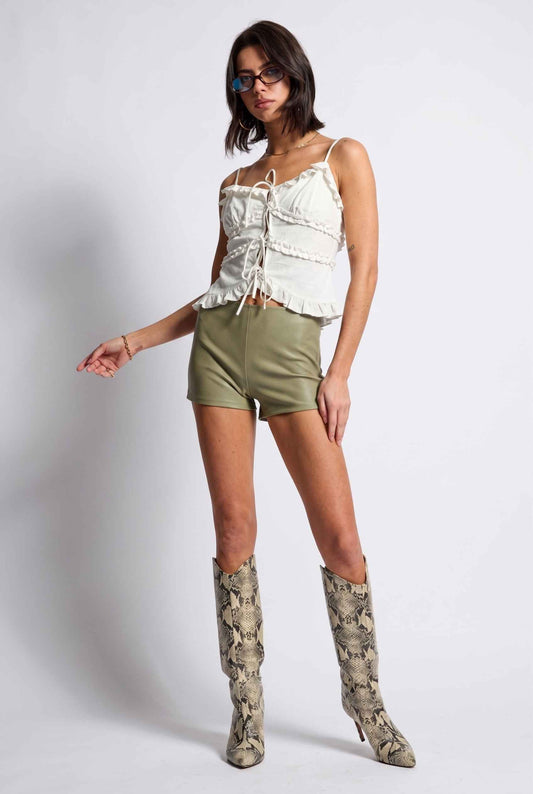 Model wearing Camille Ruffle Tie-Front Top in White Tiered Sleeveless Blouse paired with micro shorts and tall heeled boots