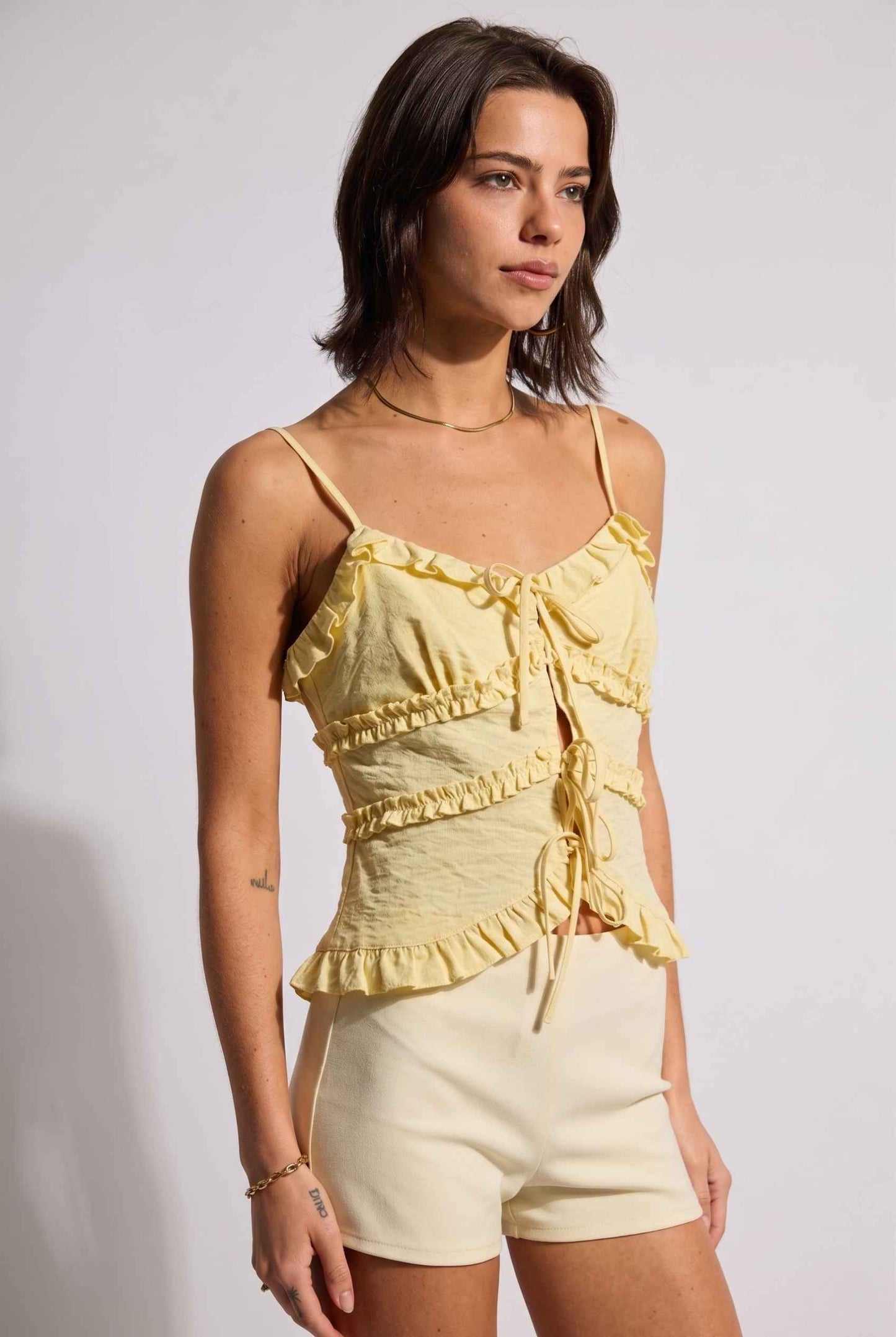 Model wearing Camille Ruffle Tie-Front Top in Yellow Tiered Sleeveless Blouse paired with micro shorts close side