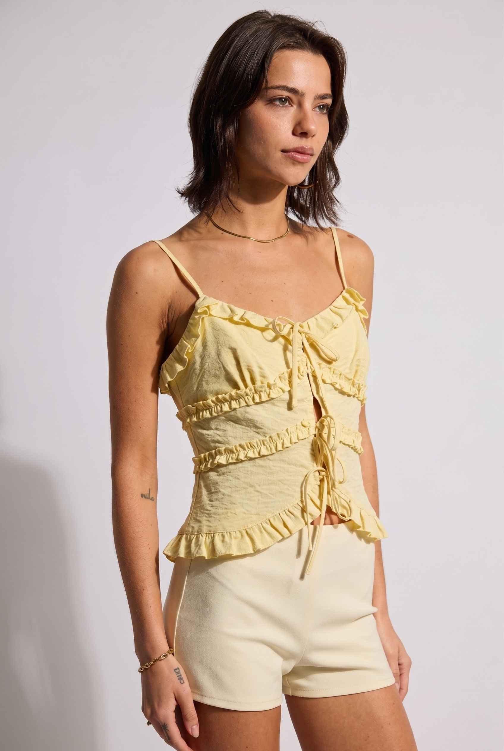 Model wearing Camille Ruffle Tie-Front Top in Yellow Tiered Sleeveless Blouse paired with micro shorts close side