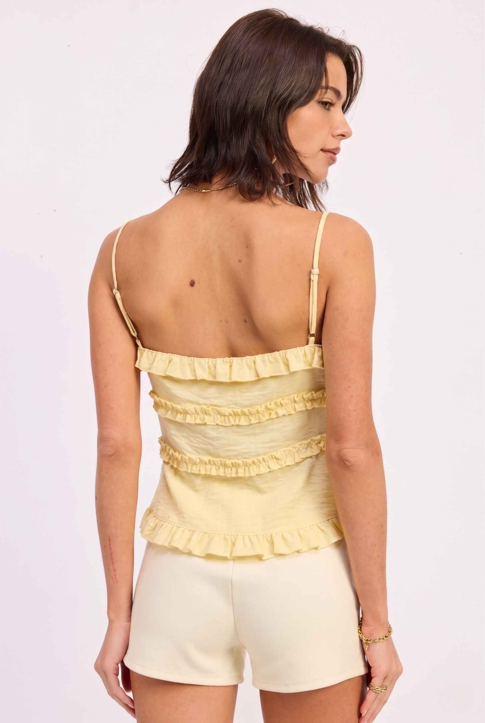 Model wearing Camille Ruffle Tie-Front Top in Yellow Tiered Sleeveless Blouse paired with micro shorts close back view