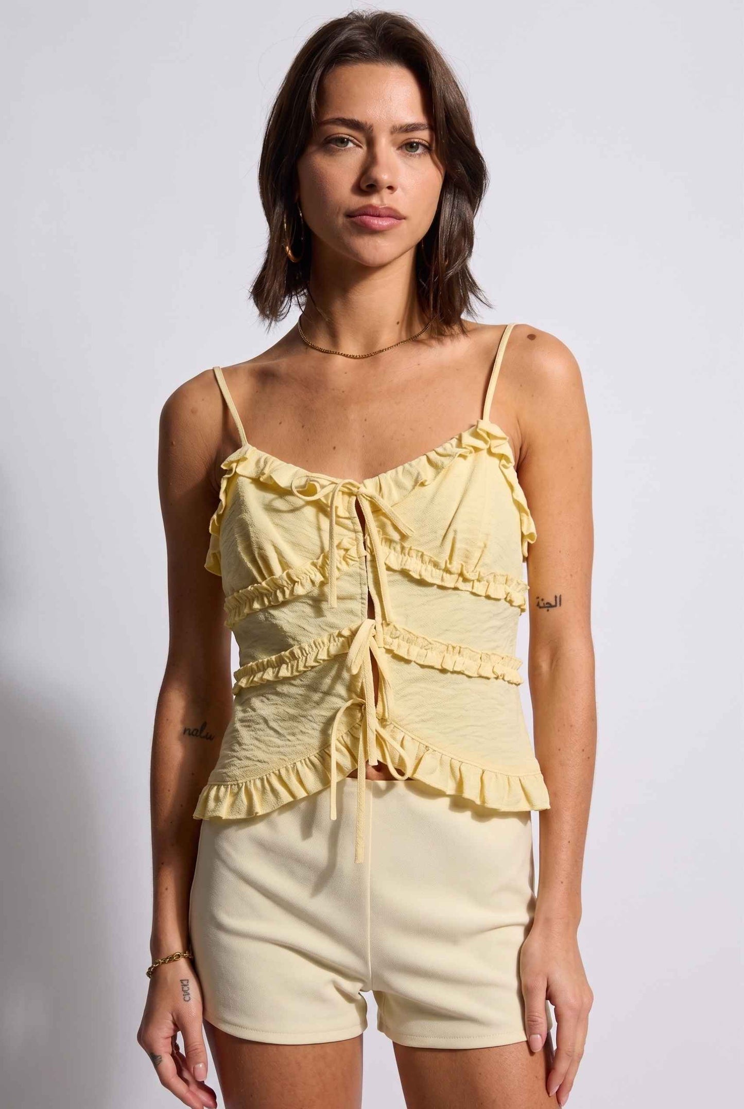 Model wearing Camille Ruffle Tie-Front Top in Yellow Tiered Sleeveless Blouse paired with micro shorts close up delicate ruffles