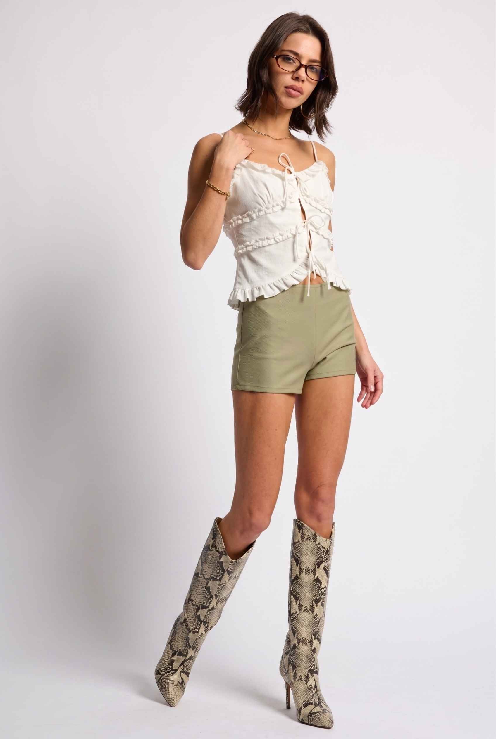 Model wearing Camille Ruffle Tie-Front Top in White Tiered Sleeveless Blouse paired with micro shorts and tall heeled boots