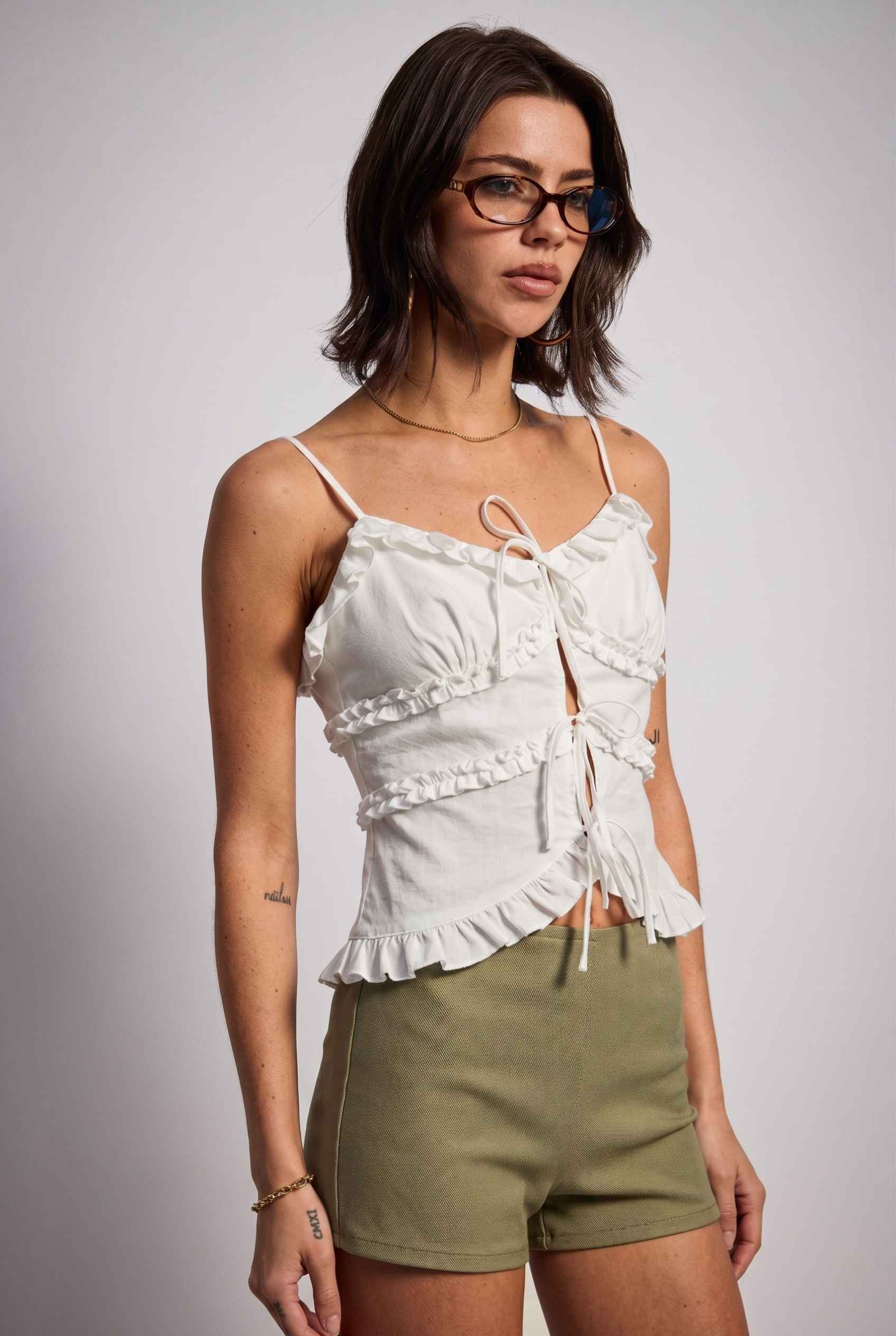 Model wearing Camille Ruffle Tie-Front Top in White Tiered Sleeveless Blouse paired with micro shorts  close up side