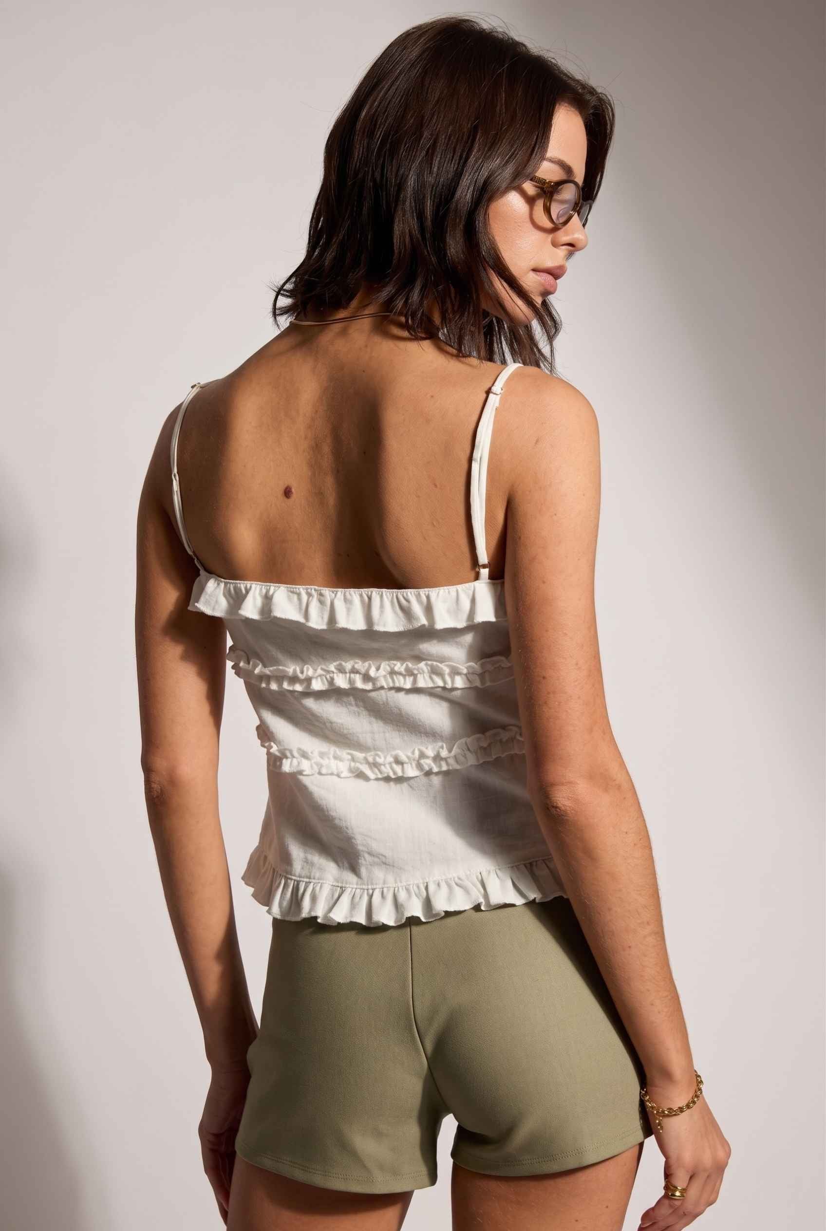 Model wearing Camille Ruffle Tie-Front Top in White Tiered Sleeveless Blouse paired with micro shorts close back view