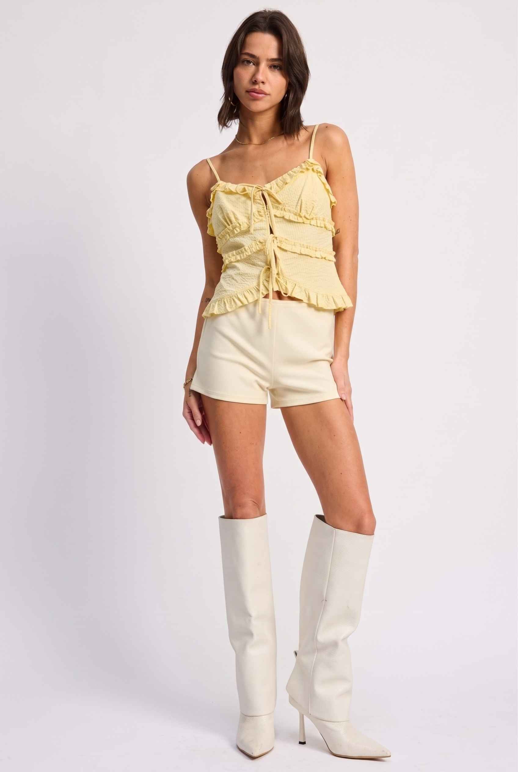 Model wearing Camille Ruffle Tie-Front Top in Yellow Tiered Sleeveless Blouse paired with micro shorts and tall heeled boots