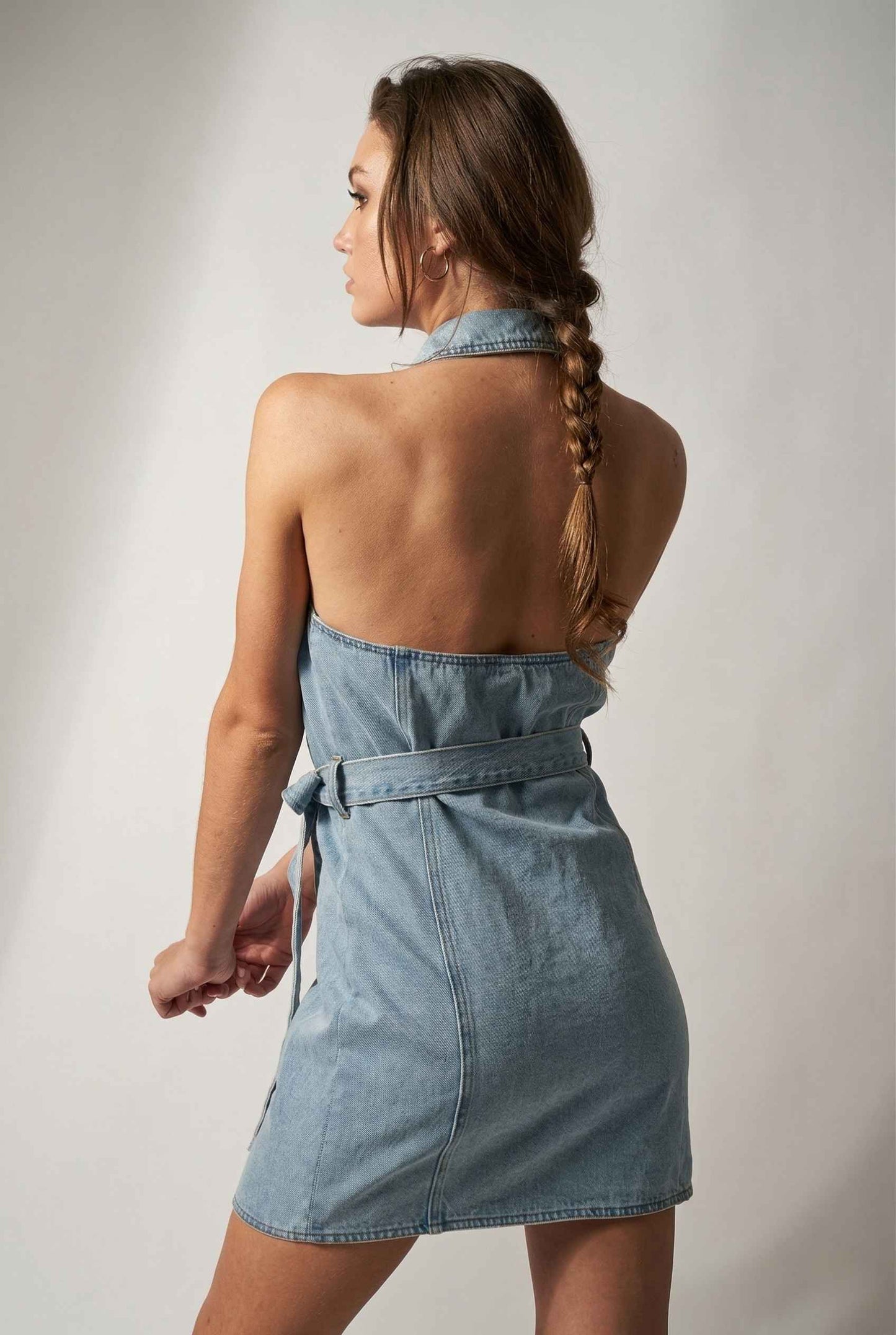 Model wearing Cassidy Mini in Light Wash Denim Button-Front Dress halter back open detail