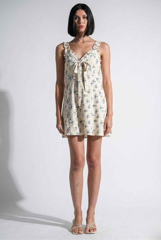 Woman wearing a Cecily Mini Ivory Floral Bow Tie Dress against a white background
