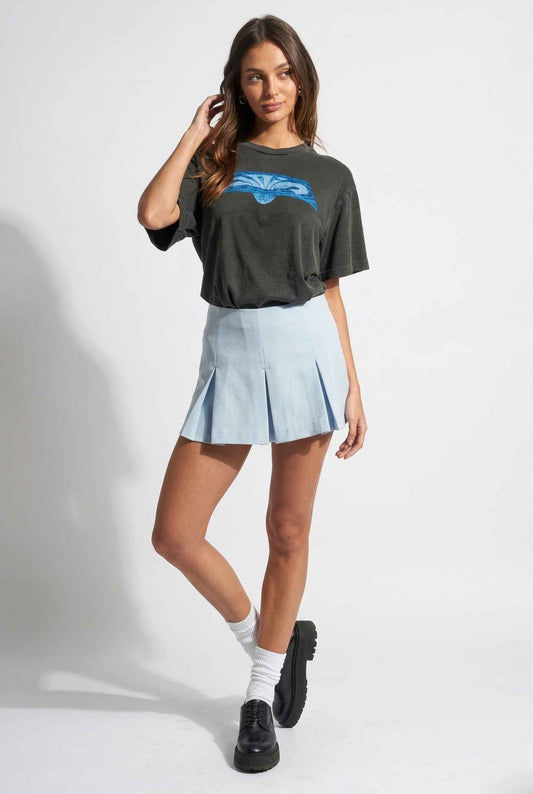 Woman wearing a dark green oversized t-shirt with a blue graphic and a Celeste Skort Baby Blue Pleated Silk-Blend Mini Skort on a white background
