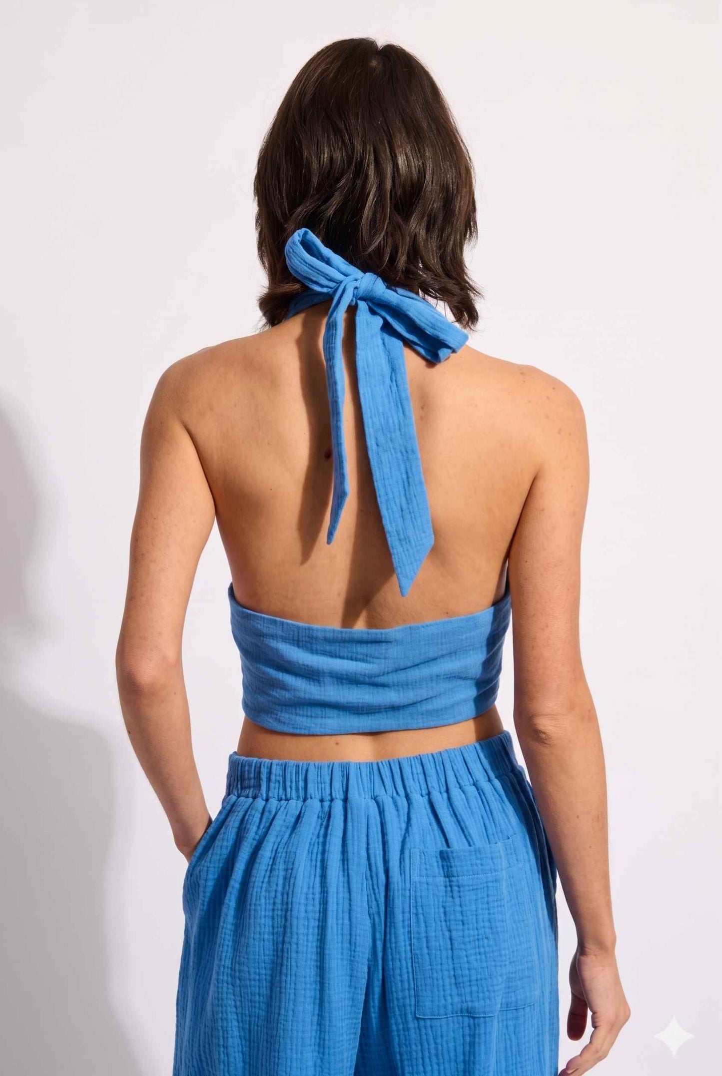 Model wearing Celine Gauze Halter Crop Top 100% Cotton Tie-Front Top in Blue paired with matching high waisted pants tie back detail