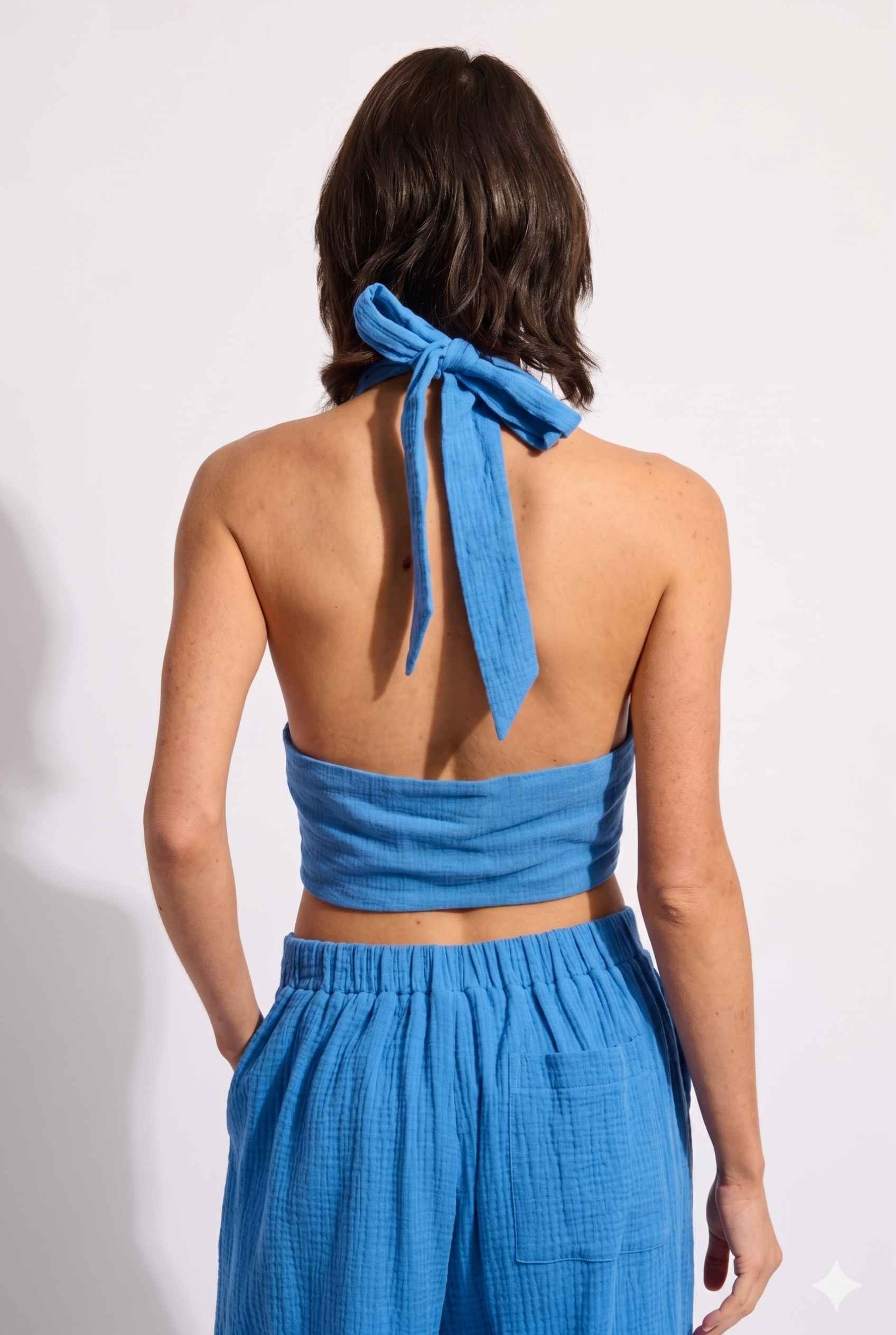 Model wearing Celine Gauze Halter Crop Top 100% Cotton Tie-Front Top in Blue paired with matching high waisted pants tie back detail