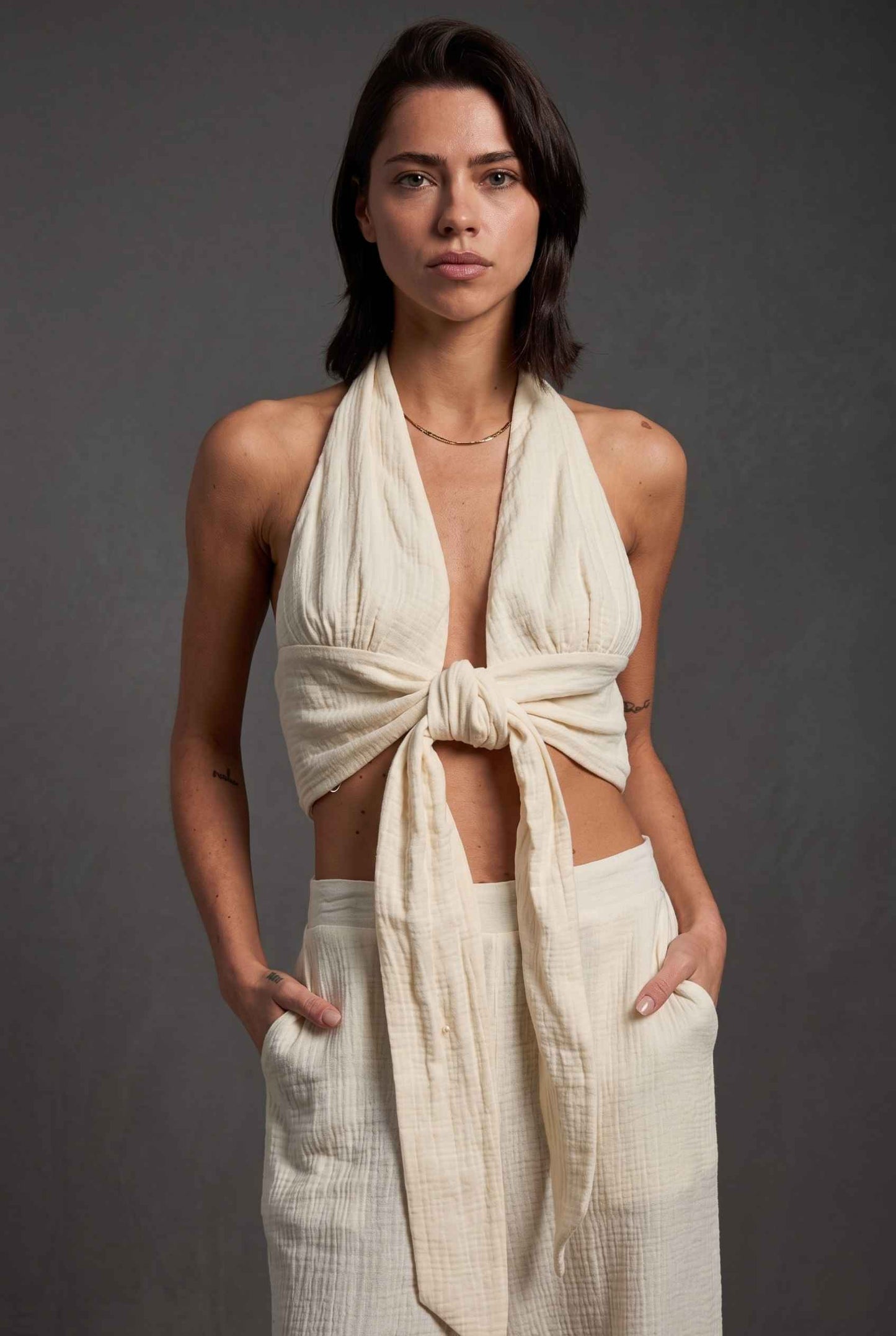 Model wearing Celine Gauze Halter Crop Top 100% Cotton Tie-Front Top in Off White paired with matching high waisted pants large tie front and halter neckline detail
