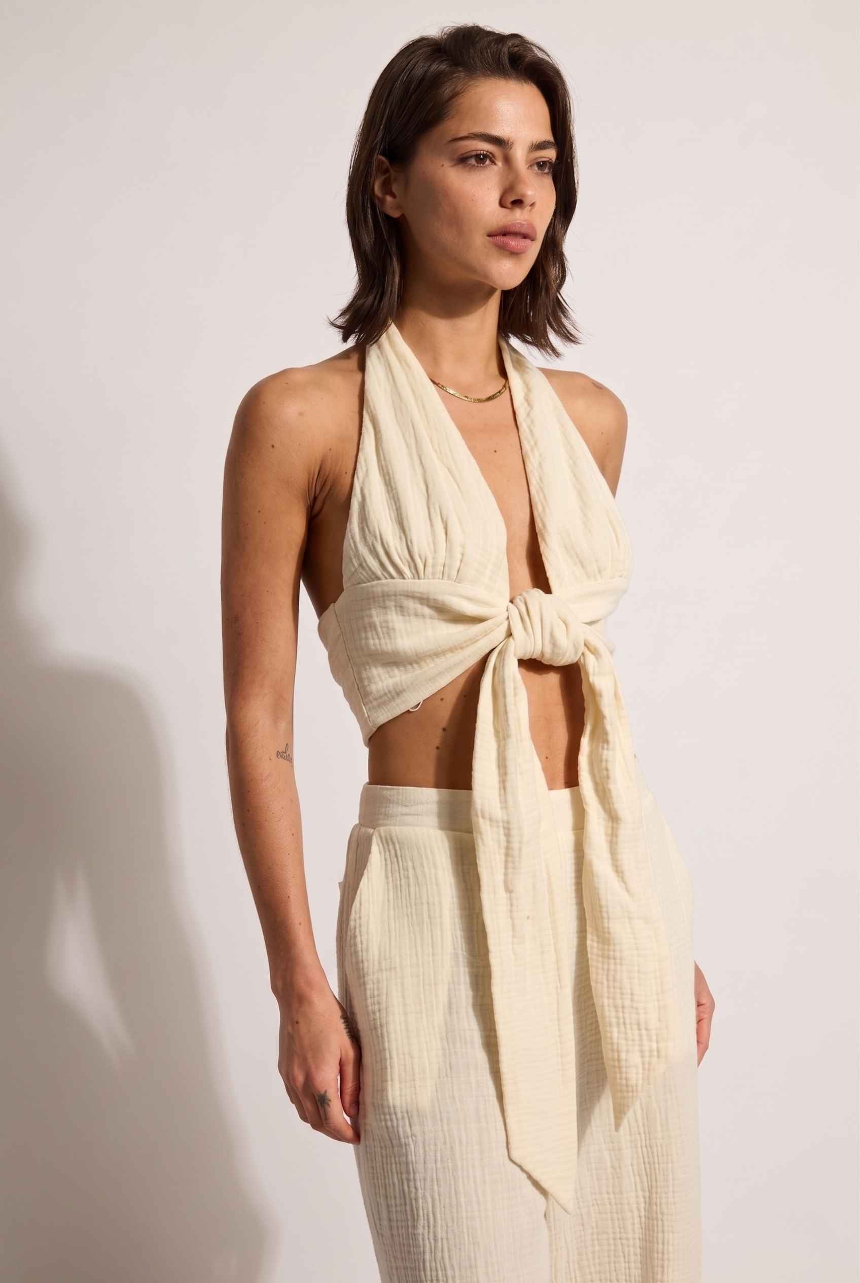 Model wearing Celine Gauze Halter Crop Top 100% Cotton Tie-Front Top in Off White paired with matching high waisted pants large tie front detail
