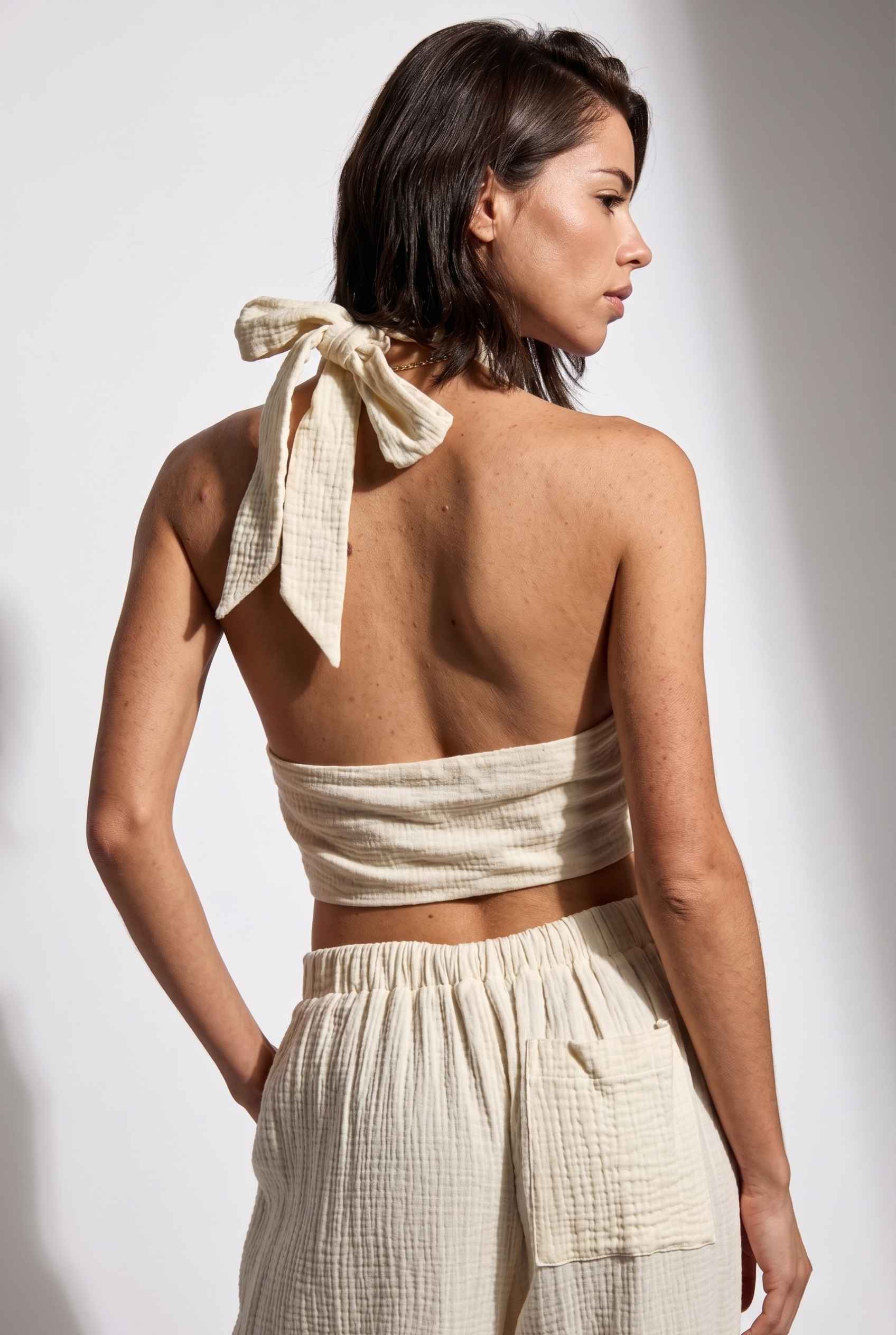 Model wearing Celine Gauze Halter Crop Top 100% Cotton Tie-Front Top in Off White paired with matching high waisted pants tie back halter detail