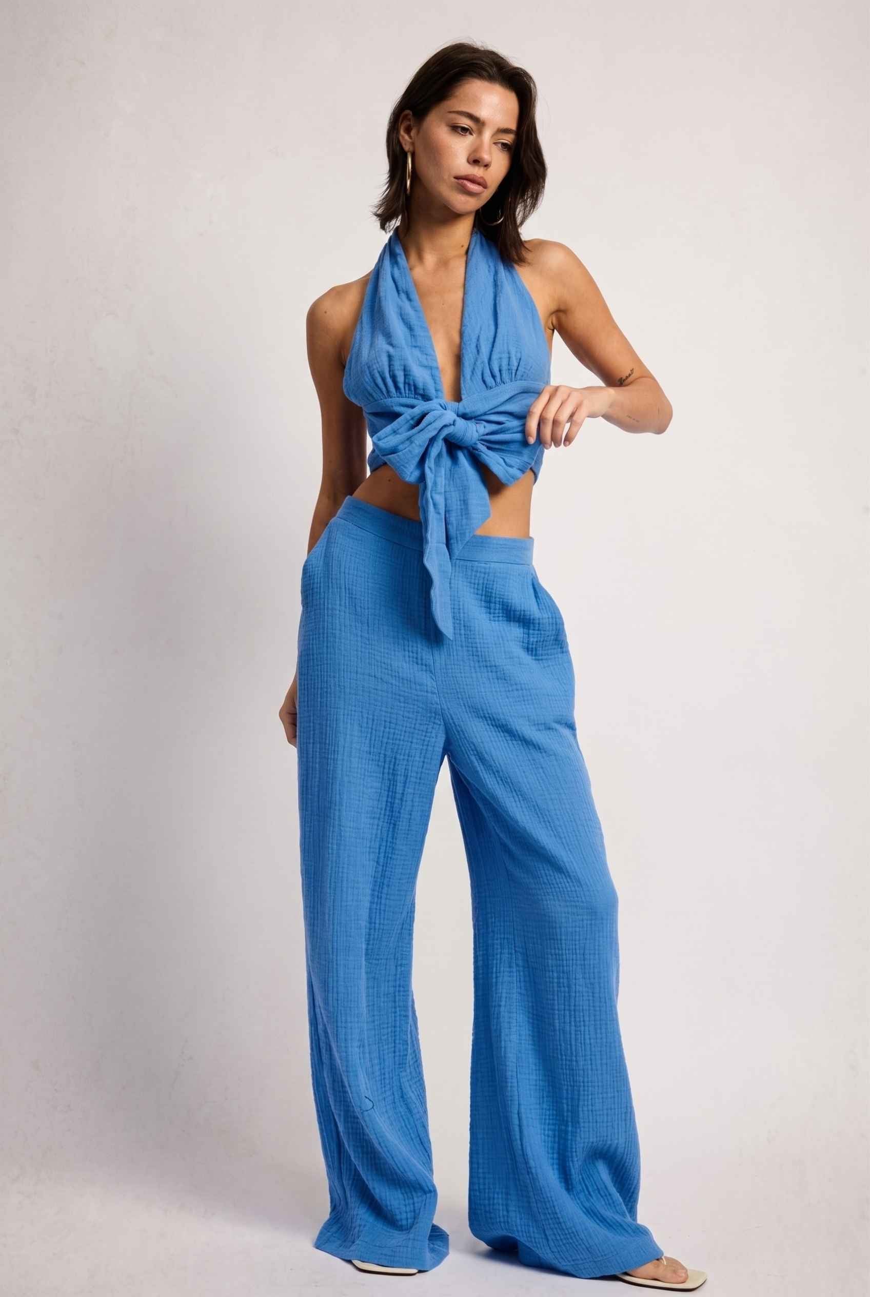 Model wearing Celine Gauze Halter Crop Top 100% Cotton Tie-Front Top in Blue paired with matching high waisted pants and sandals