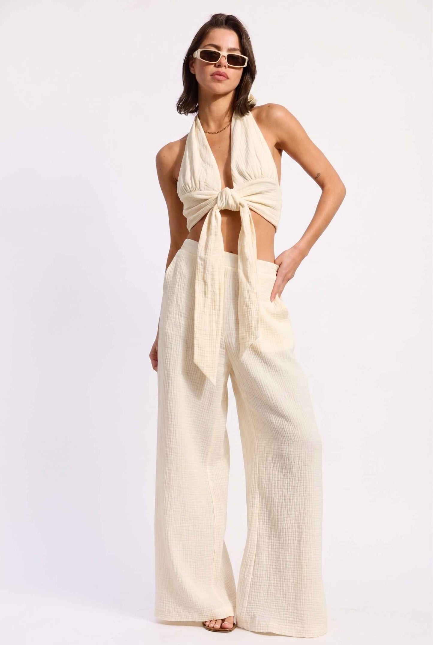 Model wearing Celine High-Waisted Gauze Pant 100% Cotton Wide-Leg Resort Pant in Off White paired with matching halter crop top and sandals