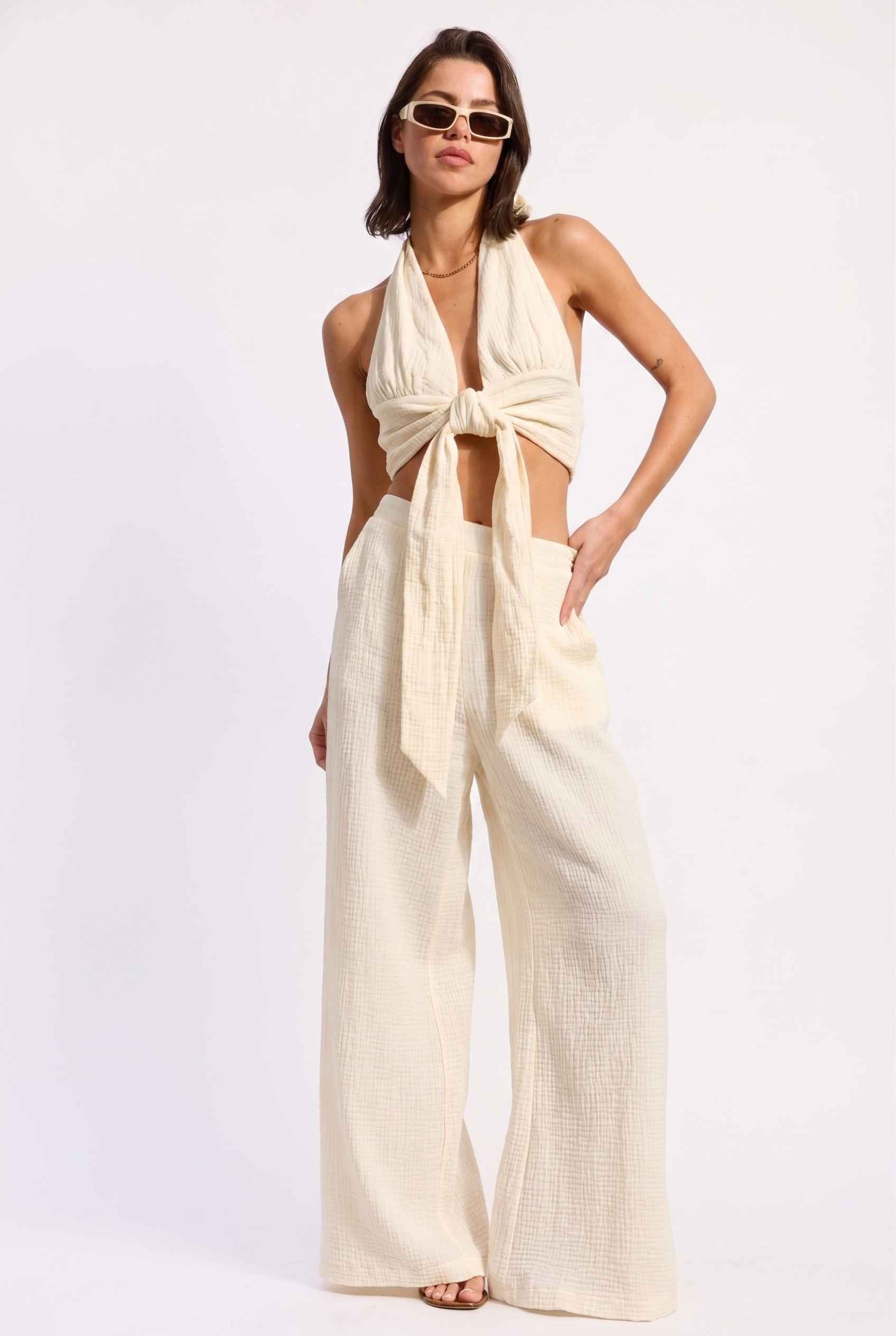 Model wearing Celine High-Waisted Gauze Pant 100% Cotton Wide-Leg Resort Pant in Off White paired with matching halter crop top and sandals