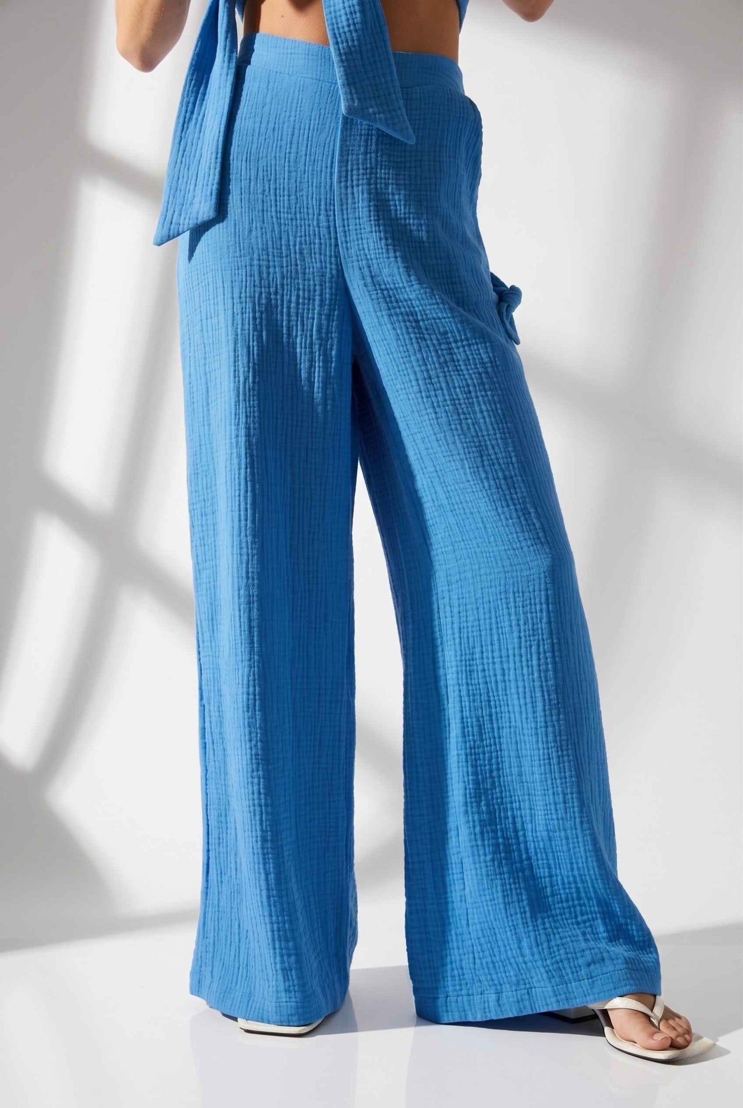 Model wearing Celine High-Waisted Gauze Pant 100% Cotton Wide-Leg Resort Pant in Blue paired with matching halter crop top and sandals