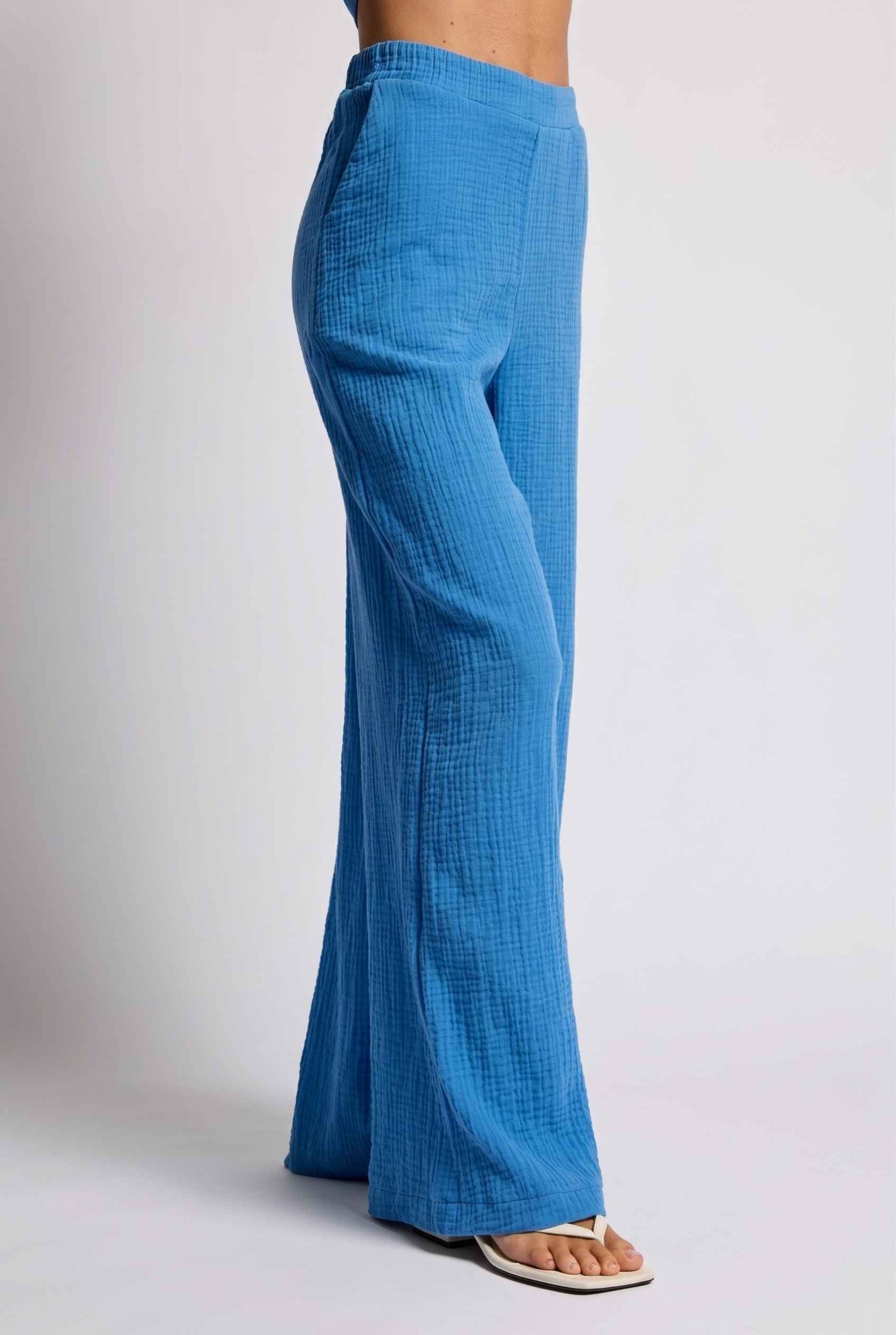 Model wearing Celine High-Waisted Gauze Pant 100% Cotton Wide-Leg Resort Pant in Blue paired with matching halter crop top and sandals