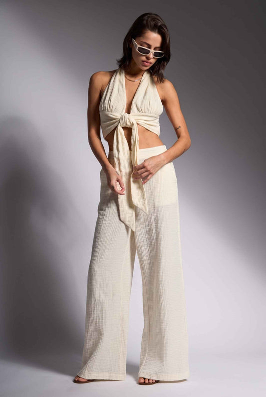Model wearing Celine High-Waisted Gauze Pant 100% Cotton Wide-Leg Resort Pant in Off White paired with matching halter crop top and sandals