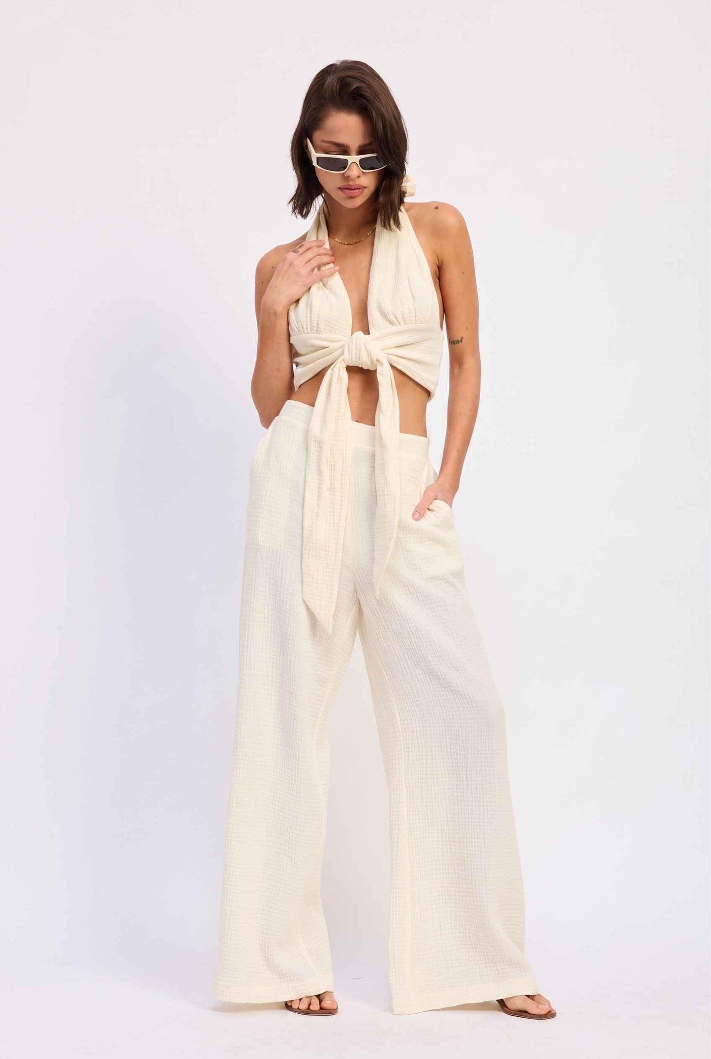 Model wearing Celine High-Waisted Gauze Pant 100% Cotton Wide-Leg Resort Pant in Off White paired with matching halter crop top and sandals