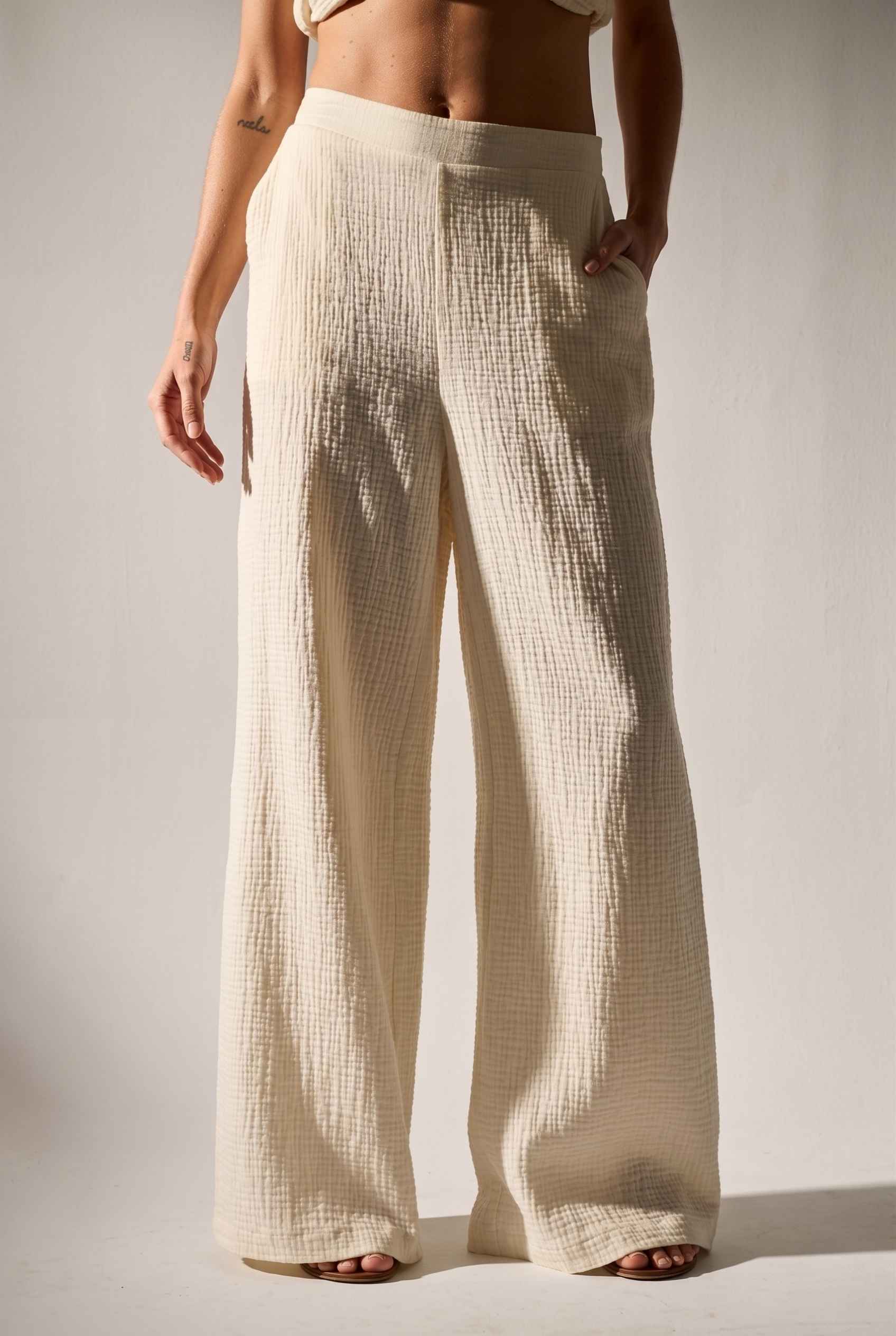 Model wearing Celine High-Waisted Gauze Pant 100% Cotton Wide-Leg Resort Pant in Off White paired with matching halter crop top and sandals
