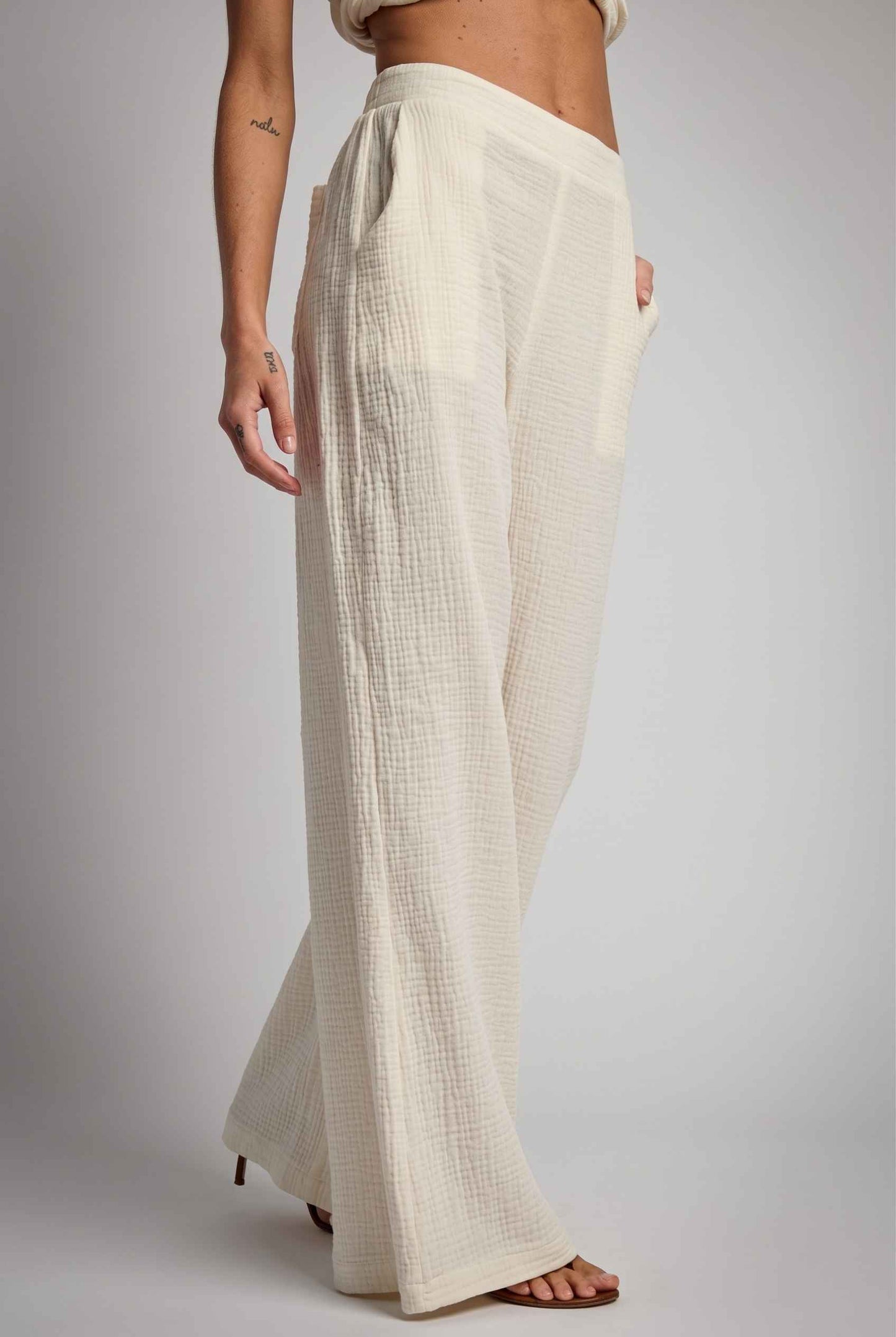 Model wearing Celine High-Waisted Gauze Pant 100% Cotton Wide-Leg Resort Pant in Off White paired with matching halter crop top and sandals